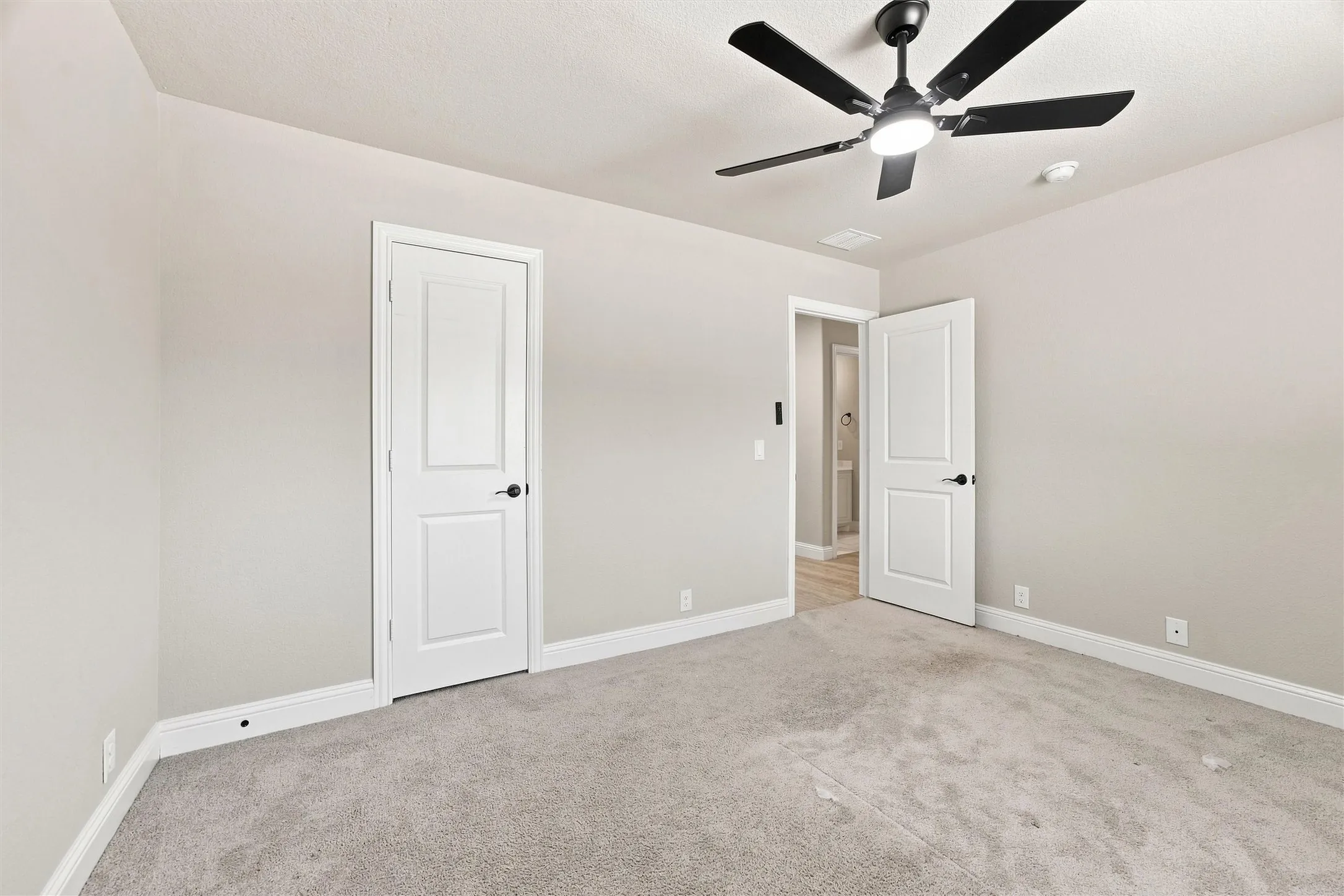 Soft gray wall paint, light-colored carpeting, white trim, and a ceiling fan with integrated lighting