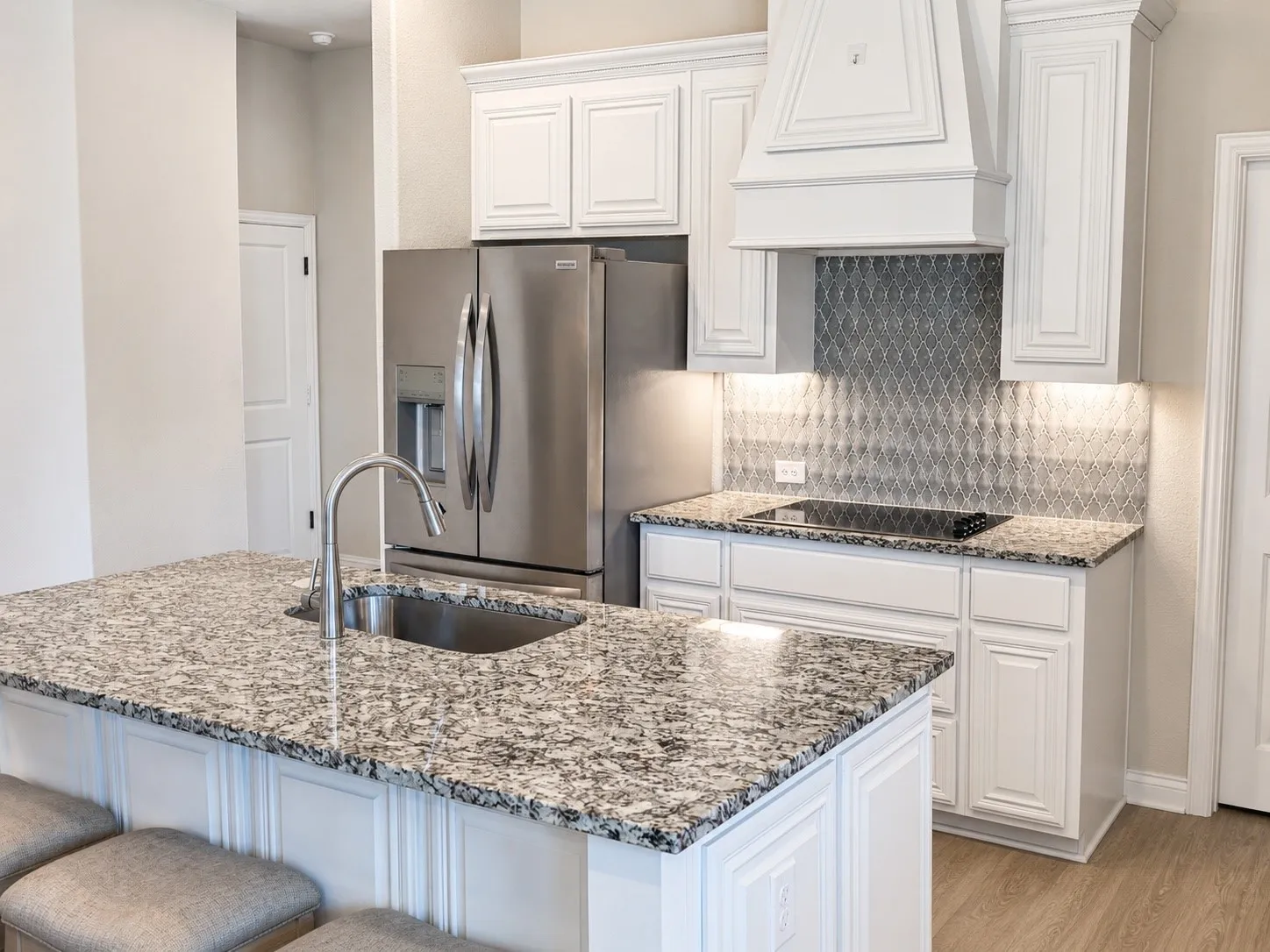 Kitchen featuring a granite island with an undermount sink and gooseneck faucet, white cabinetry, stainless steel appliances, and a mosaic tile backsplash