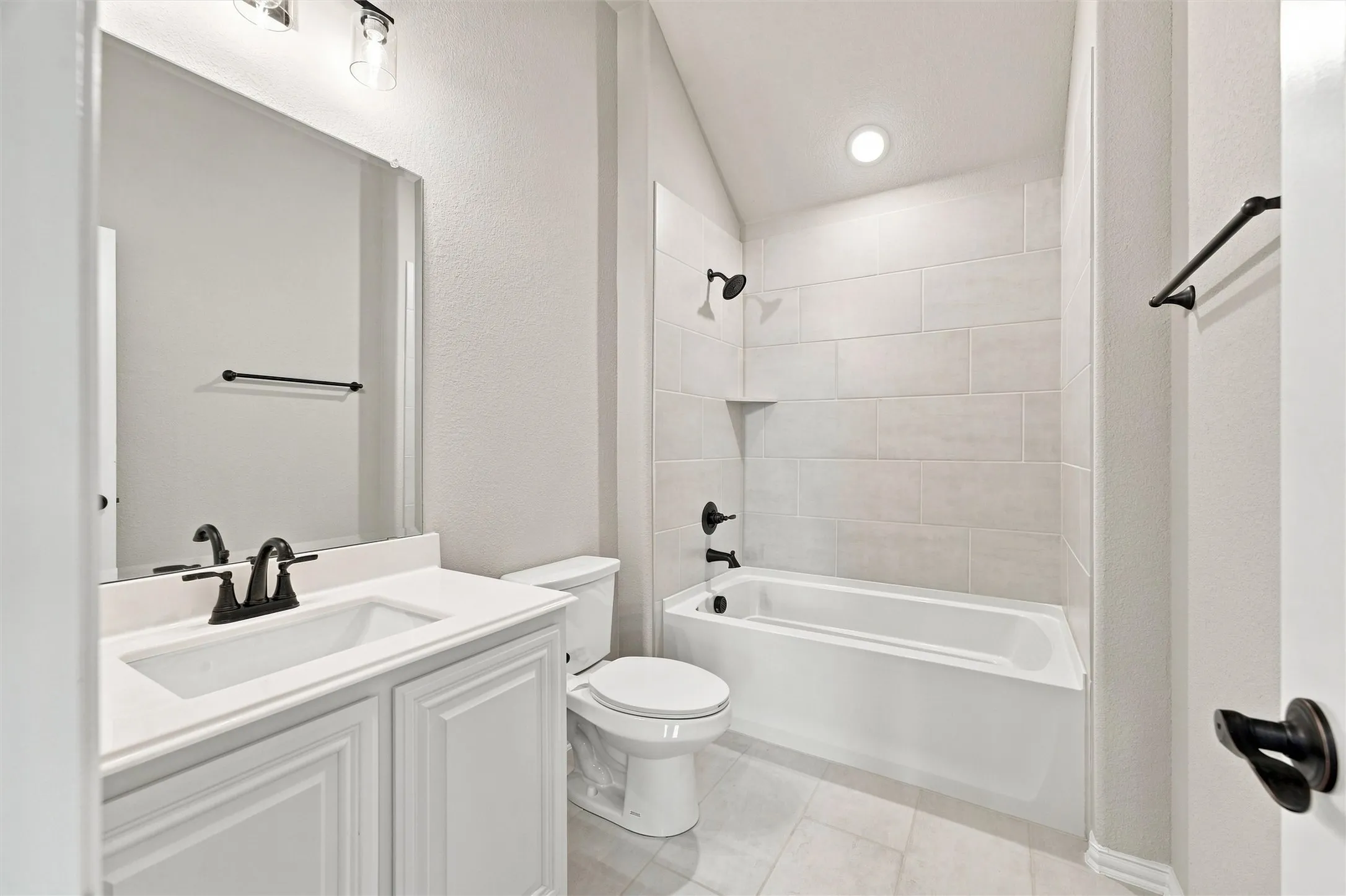 Spa-inspired bathroom featuring a white vanity with dual sinks and matte black hardware, subway tile surround, recessed lighting, and an alcove bathtub with glass enclosure and matching matte black fixtures
