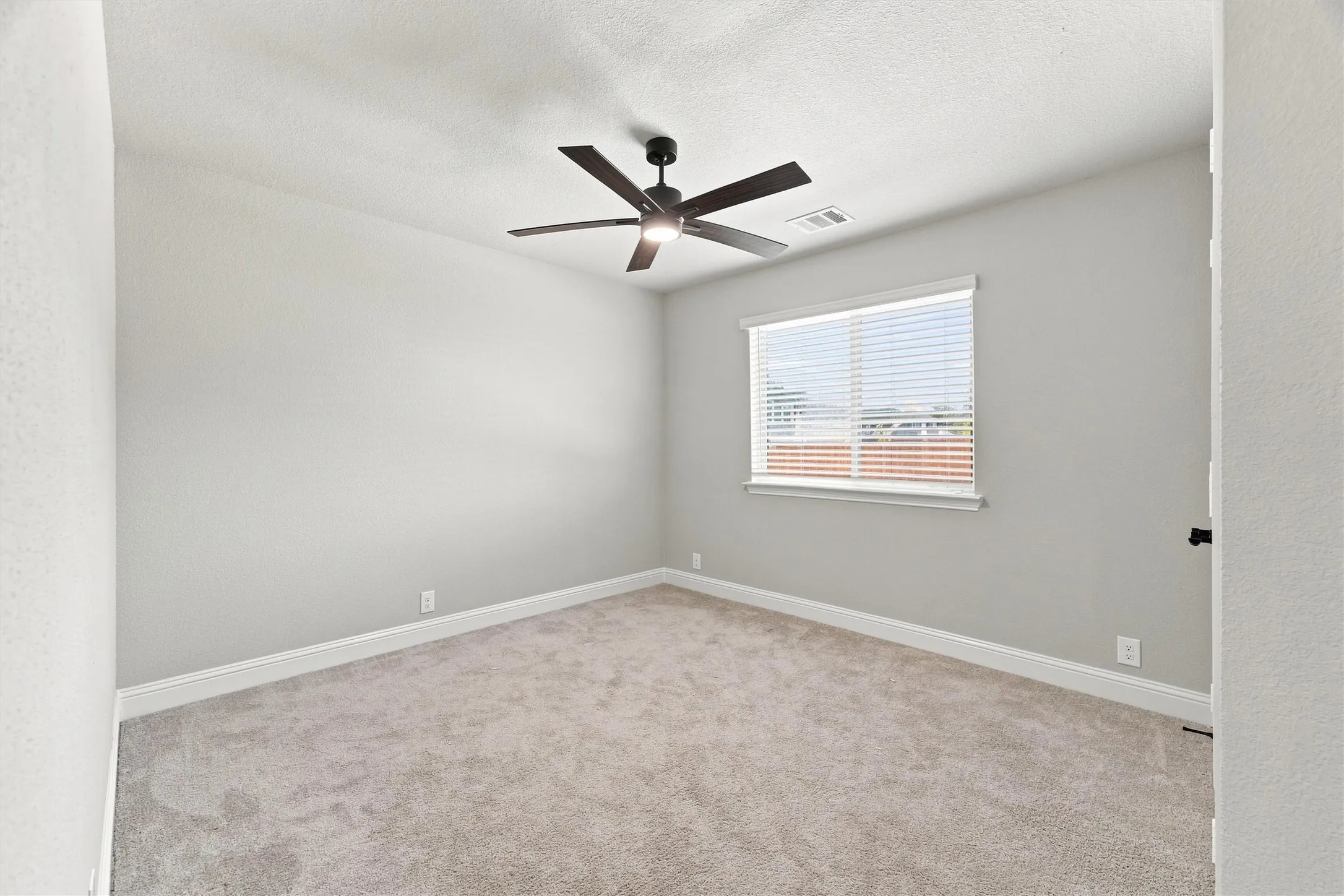 Spacious bedroom with neutral wall finishes, plush carpeting, and abundant natural light from a large window with plantation shutters