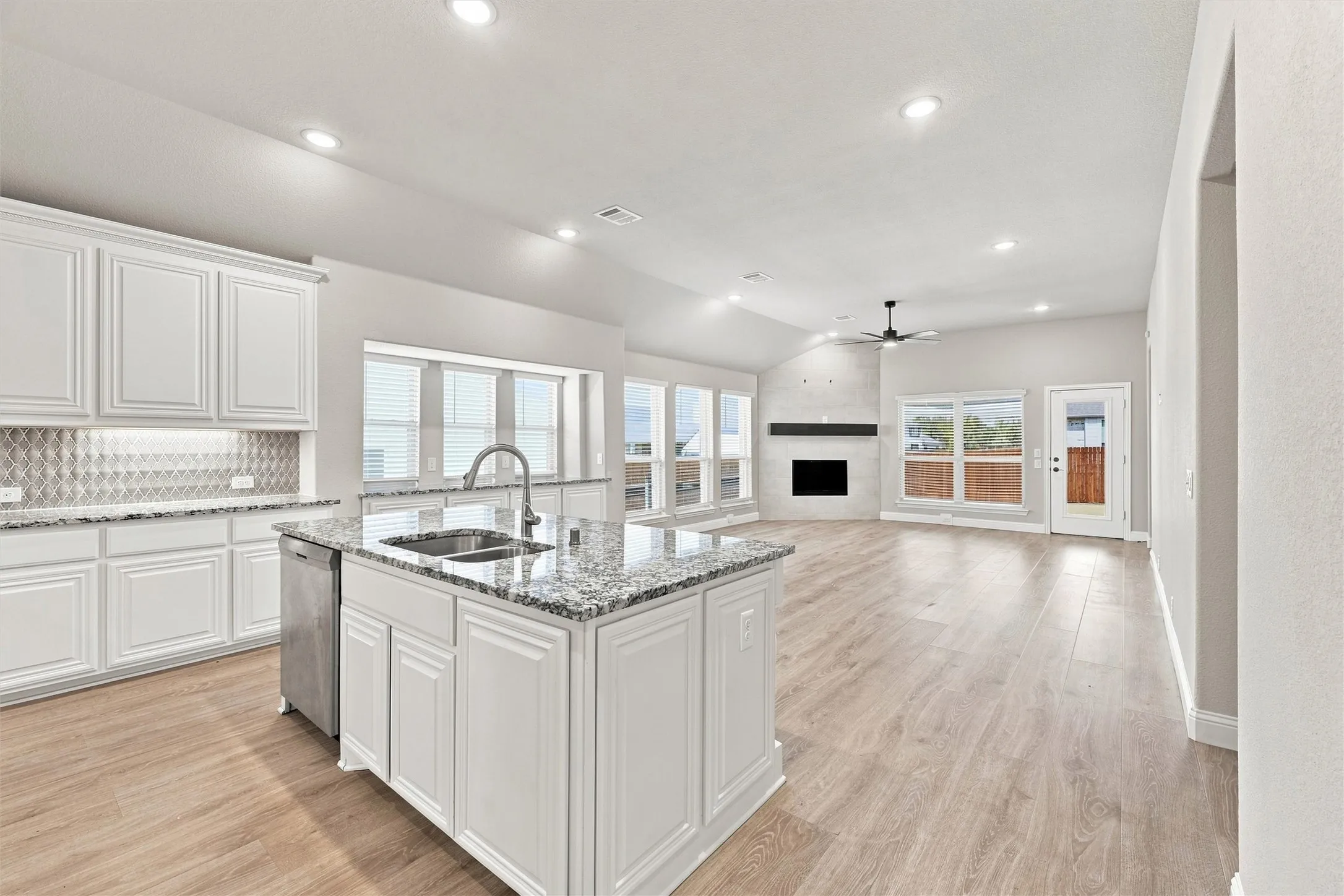 Chef's kitchen featuring white cabinetry, a large center island with waterfall countertop and undermount sink, stainless steel appliances, and geometric tile backsplash