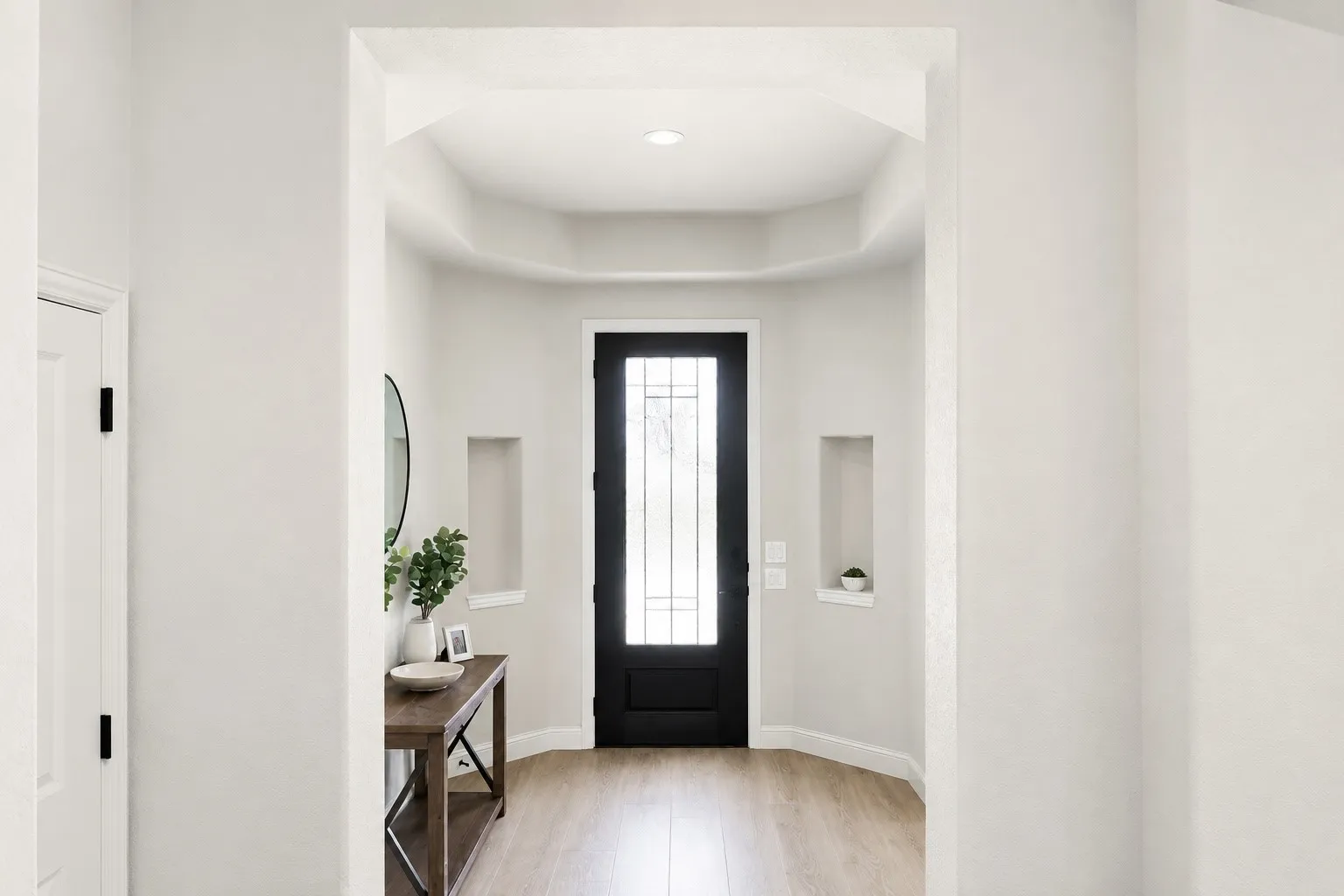 Wood-finish flooring leading to a black front door with decorative glass