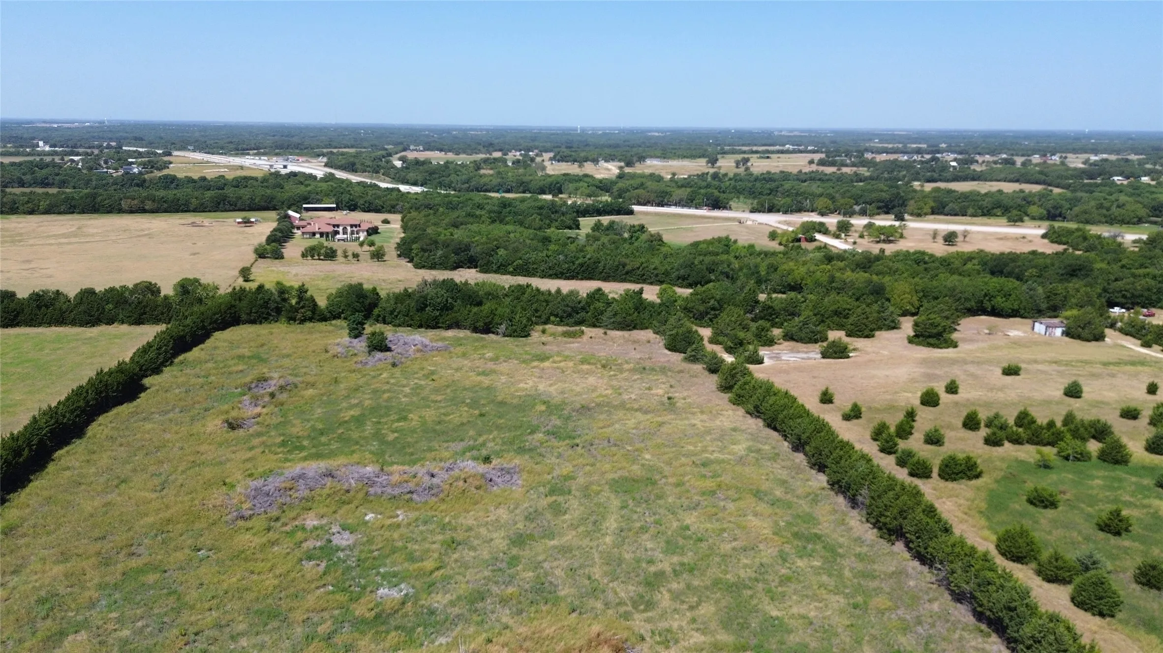 Expansive land parcel featuring open fields, natural tree lines, and a distant developed area