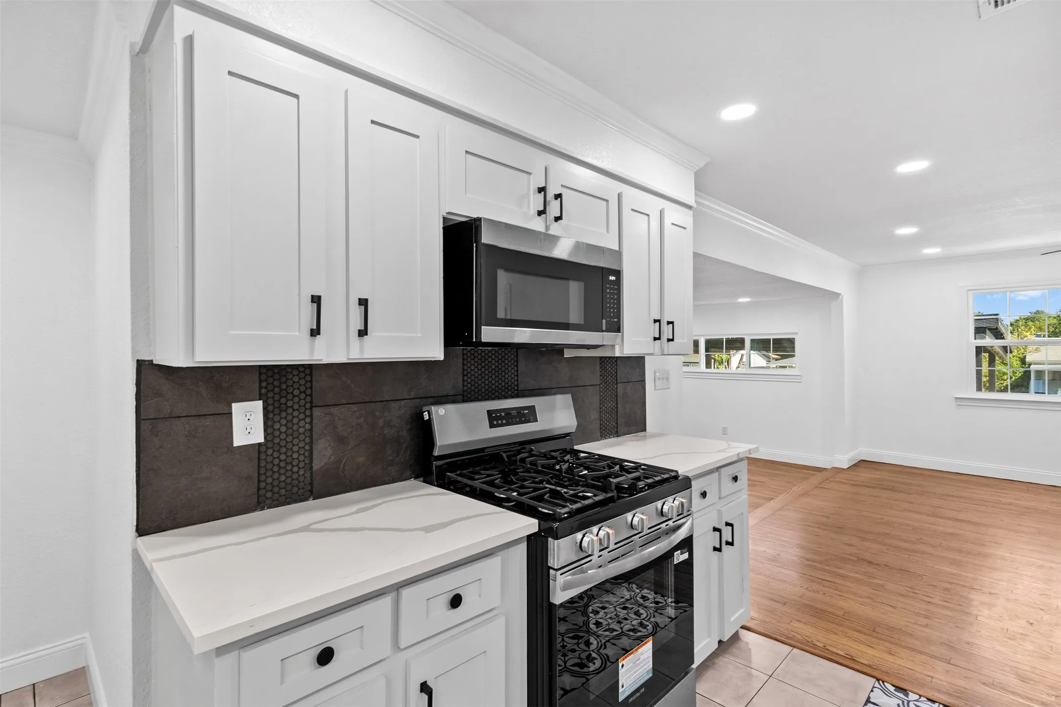 White shaker cabinetry, stainless steel appliances, quartz countertops, a dark tile backsplash, and recessed lighting