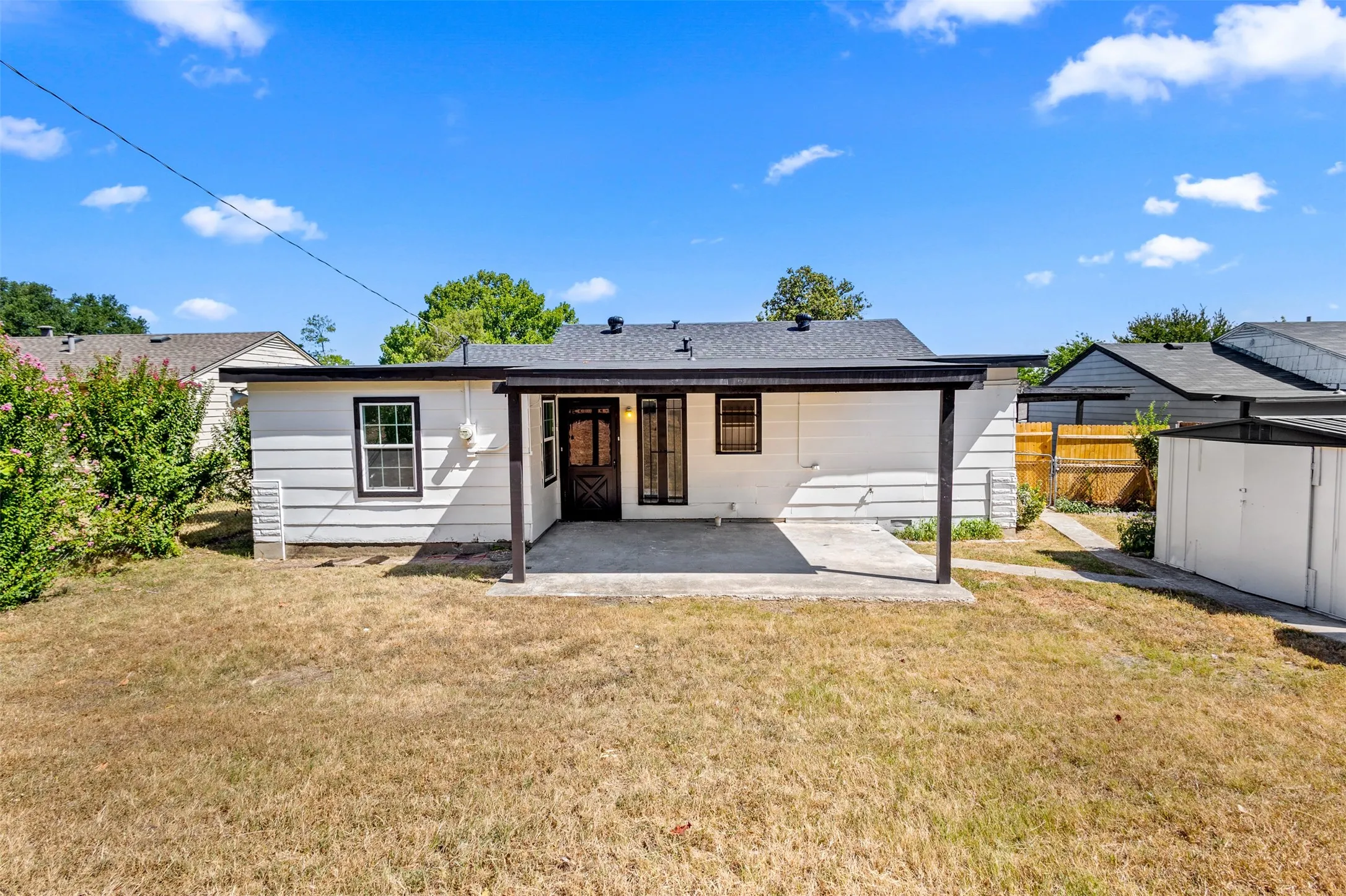 Rear exterior featuring a covered patio, concrete slab, white horizontal siding, and a dark shingle roof