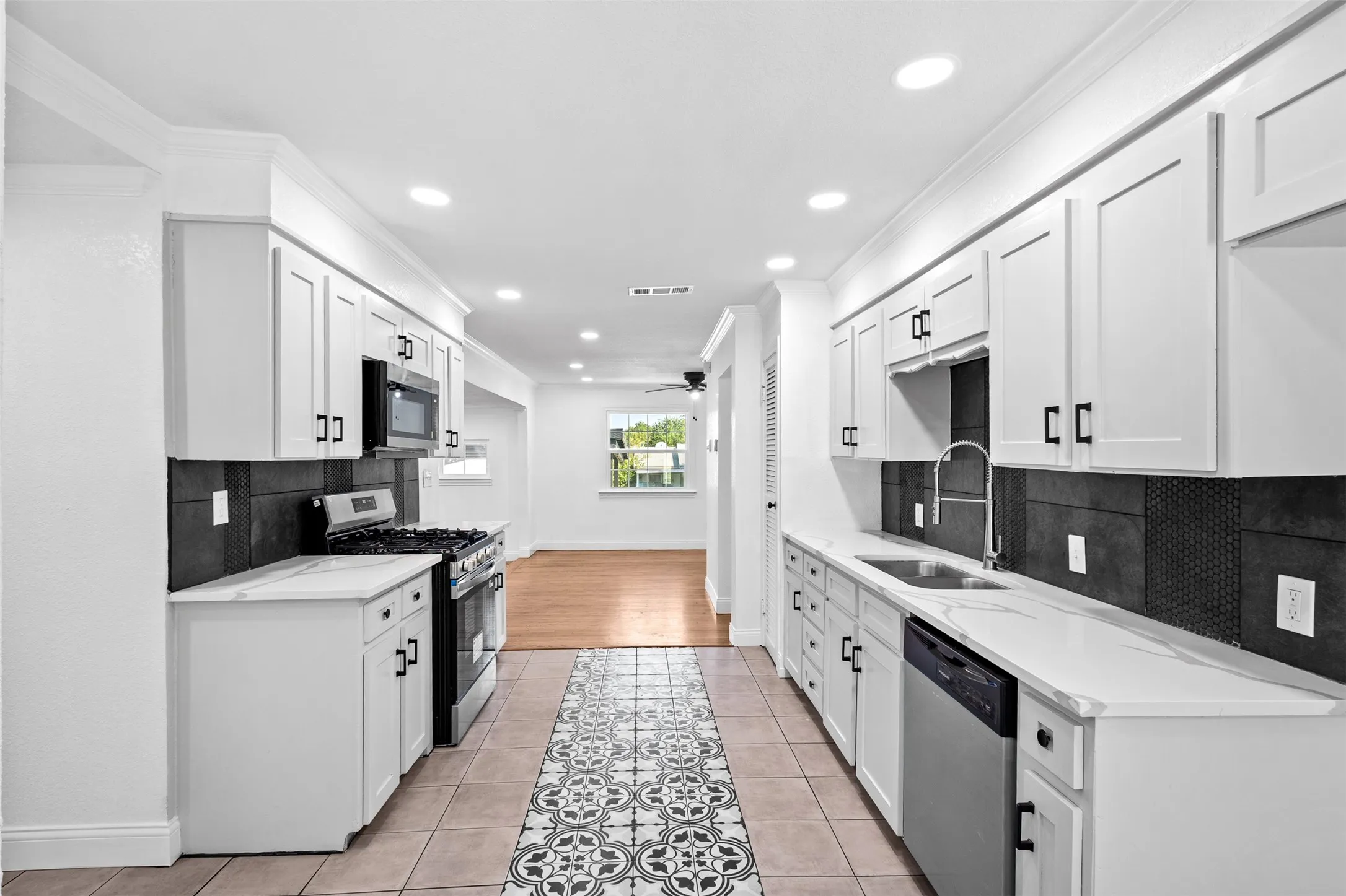 Galley kitchen featuring white cabinetry, stainless steel appliances, white countertops, and a dark tile backsplash