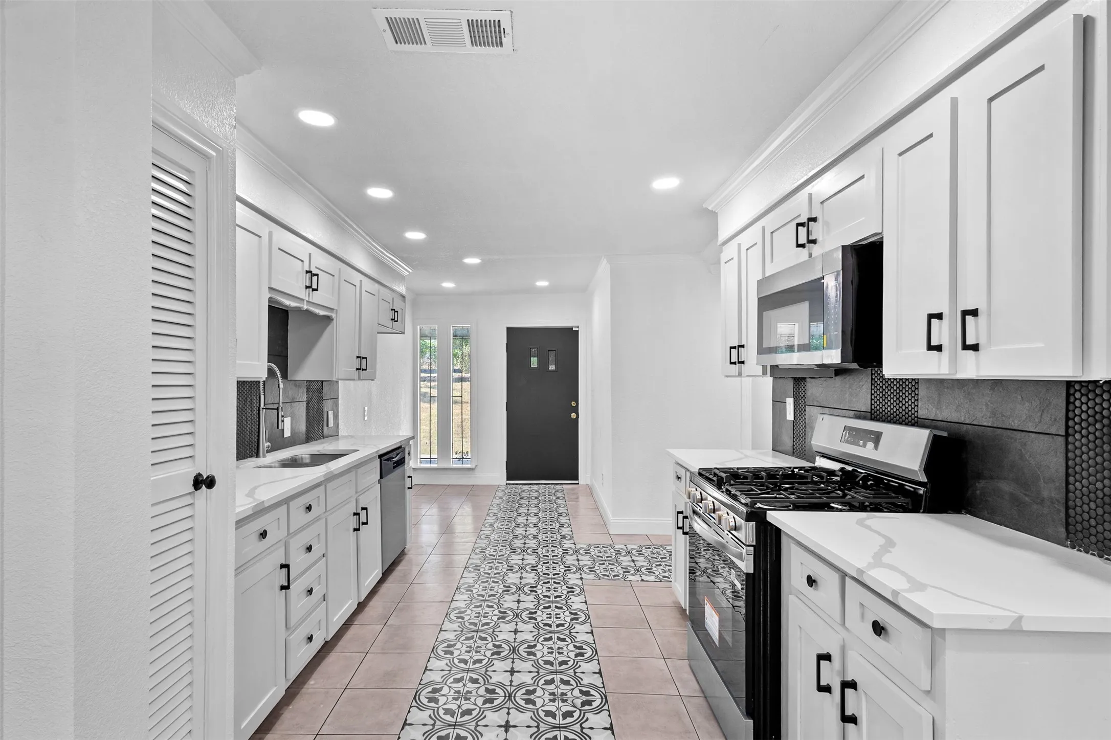 Galley kitchen featuring white cabinetry with black hardware, white countertops, stainless steel appliances, and a tiled floor