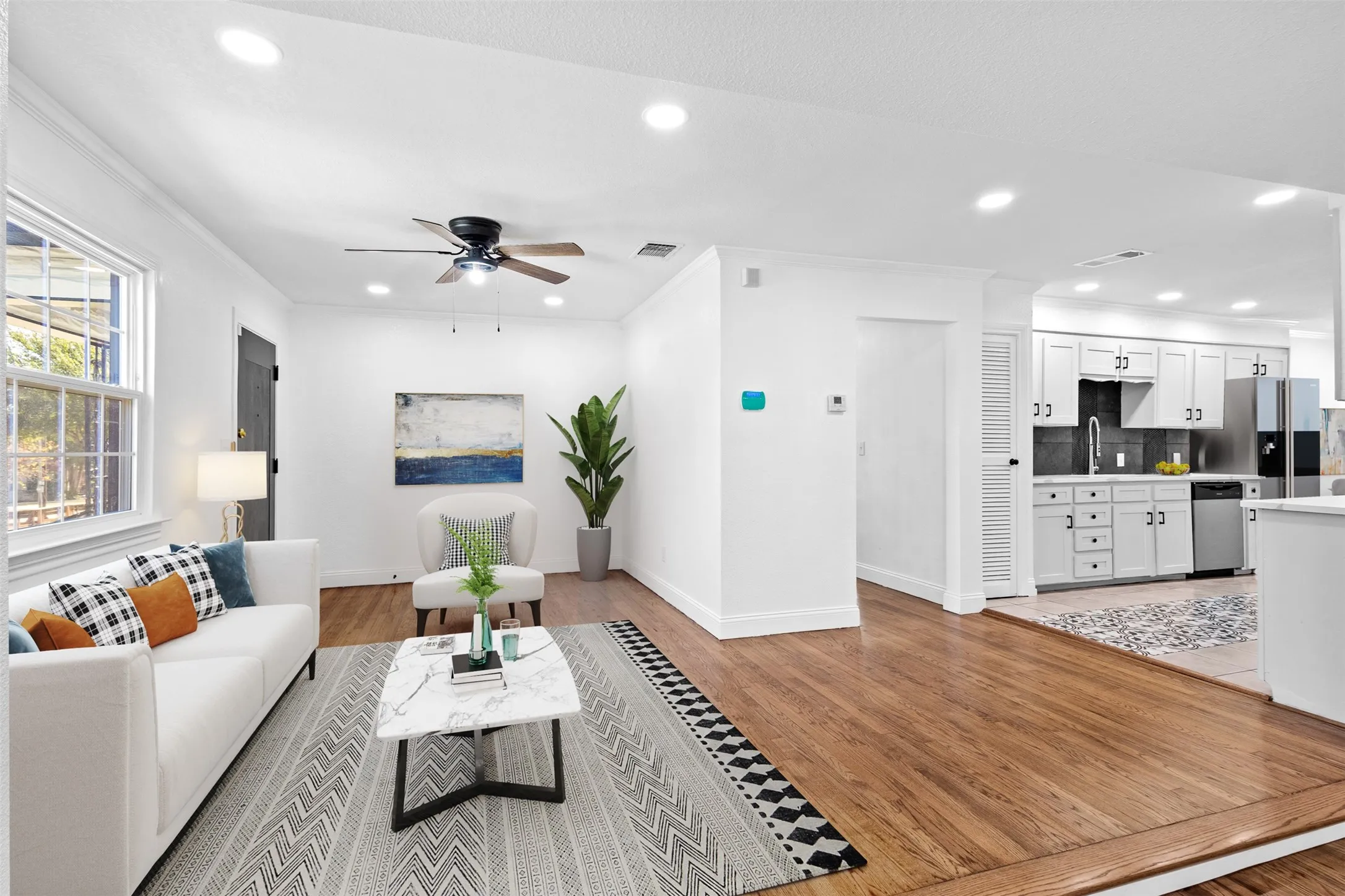 Recessed lighting, wood-finish flooring, ceiling fan, white cabinetry with dark hardware, and stainless steel appliances