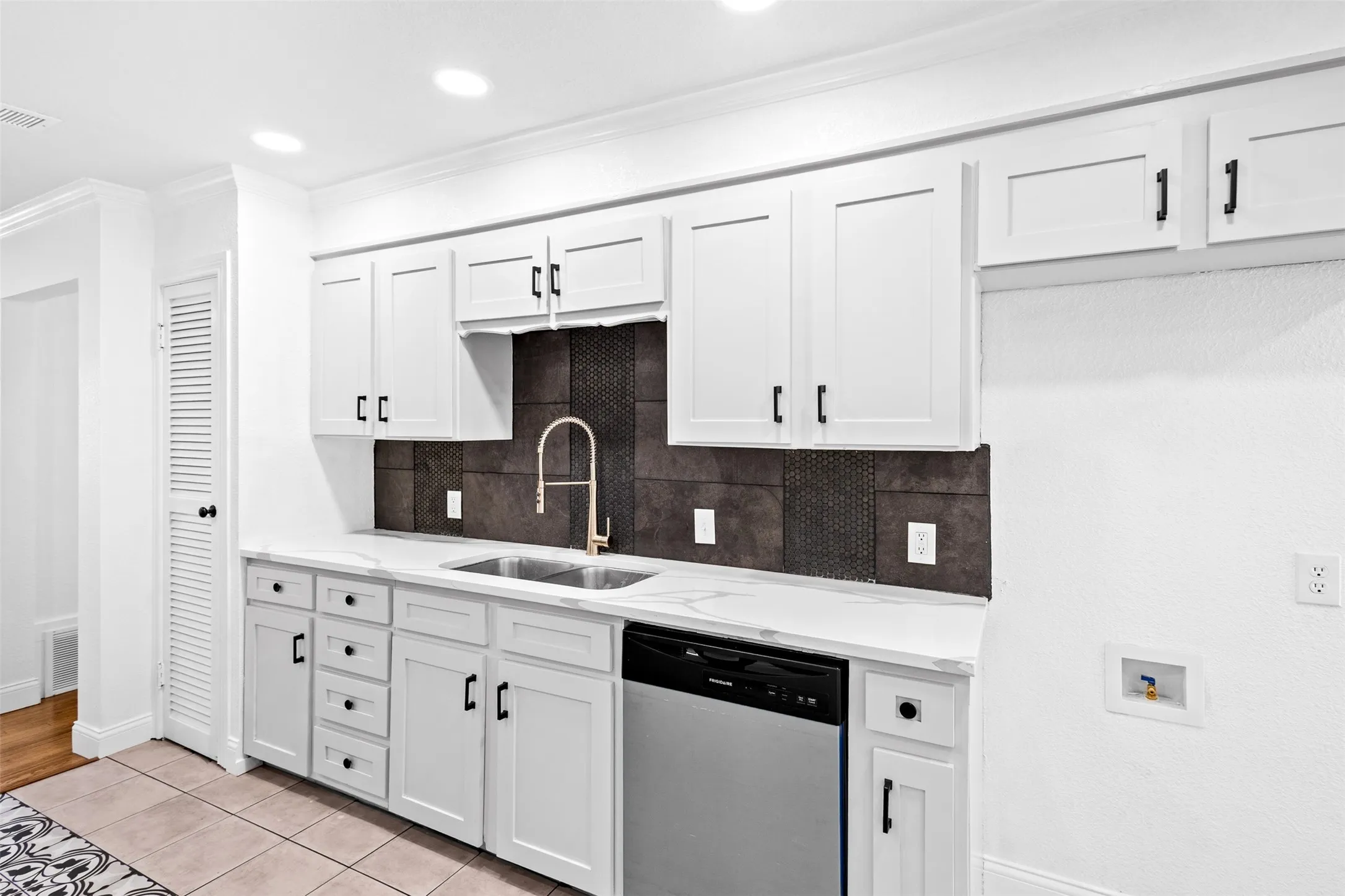 Kitchen featuring white shaker-style cabinetry, quartz-finish countertops, stainless steel sink, gold-finish gooseneck faucet, and a dark mosaic tile backsplash