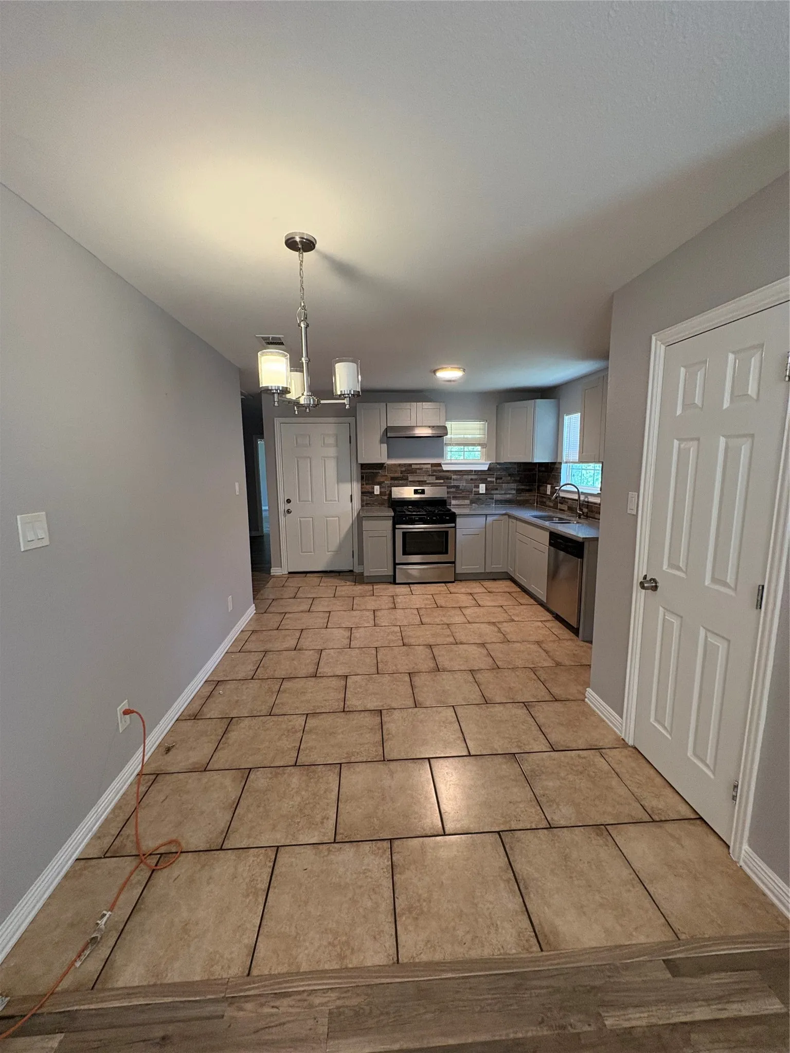 Kitchen featuring tile flooring, light gray cabinetry, stainless steel appliances, and a tiled backsplash