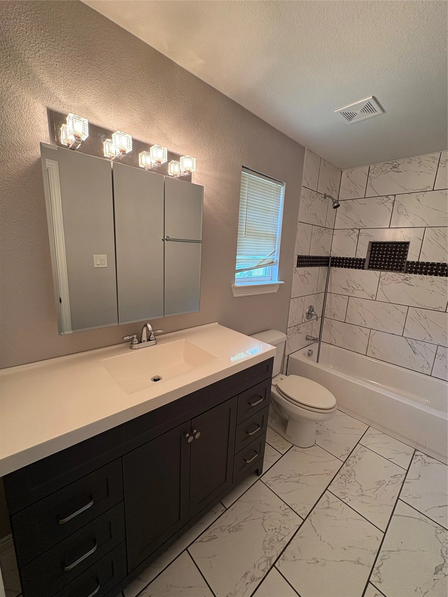 White tile flooring, a dark wood-finish vanity with an integrated sink, and a tiled shower/tub combination