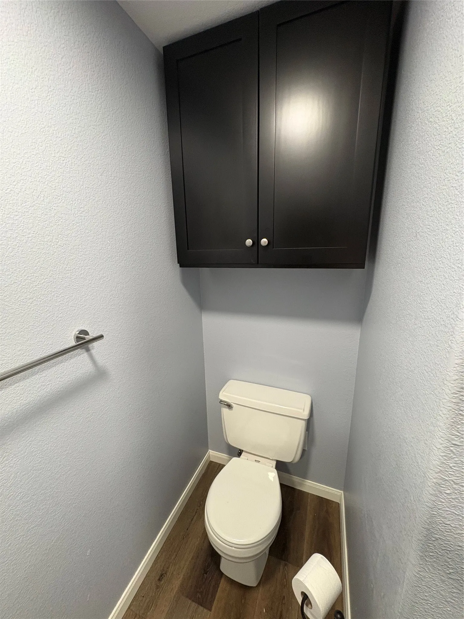 Wood-finish flooring, wall-mounted dark cabinetry, and a chrome towel bar