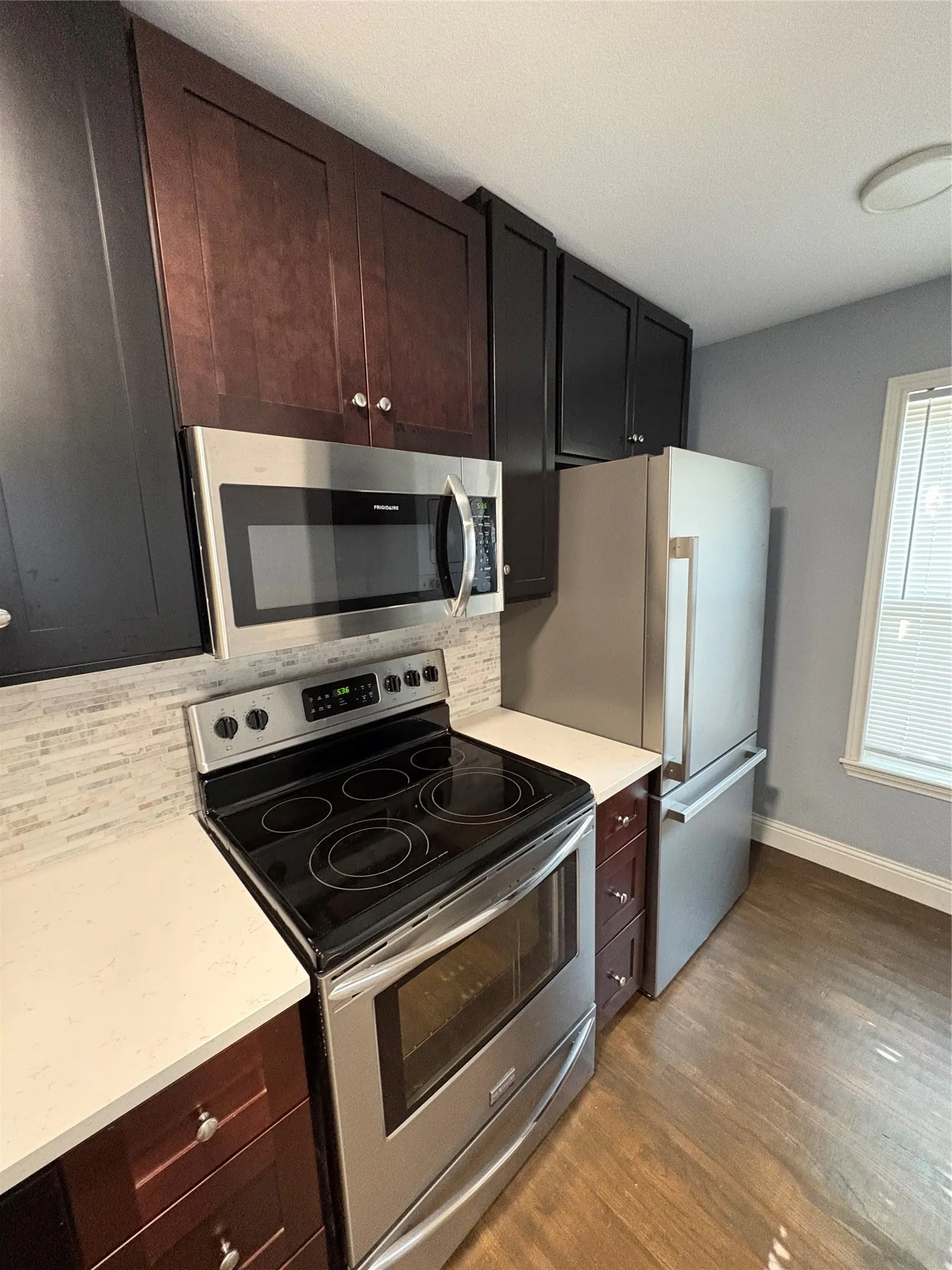 Stainless steel appliances, light-toned countertops, two-tone cabinetry, tiled backsplash, and wood-finish flooring