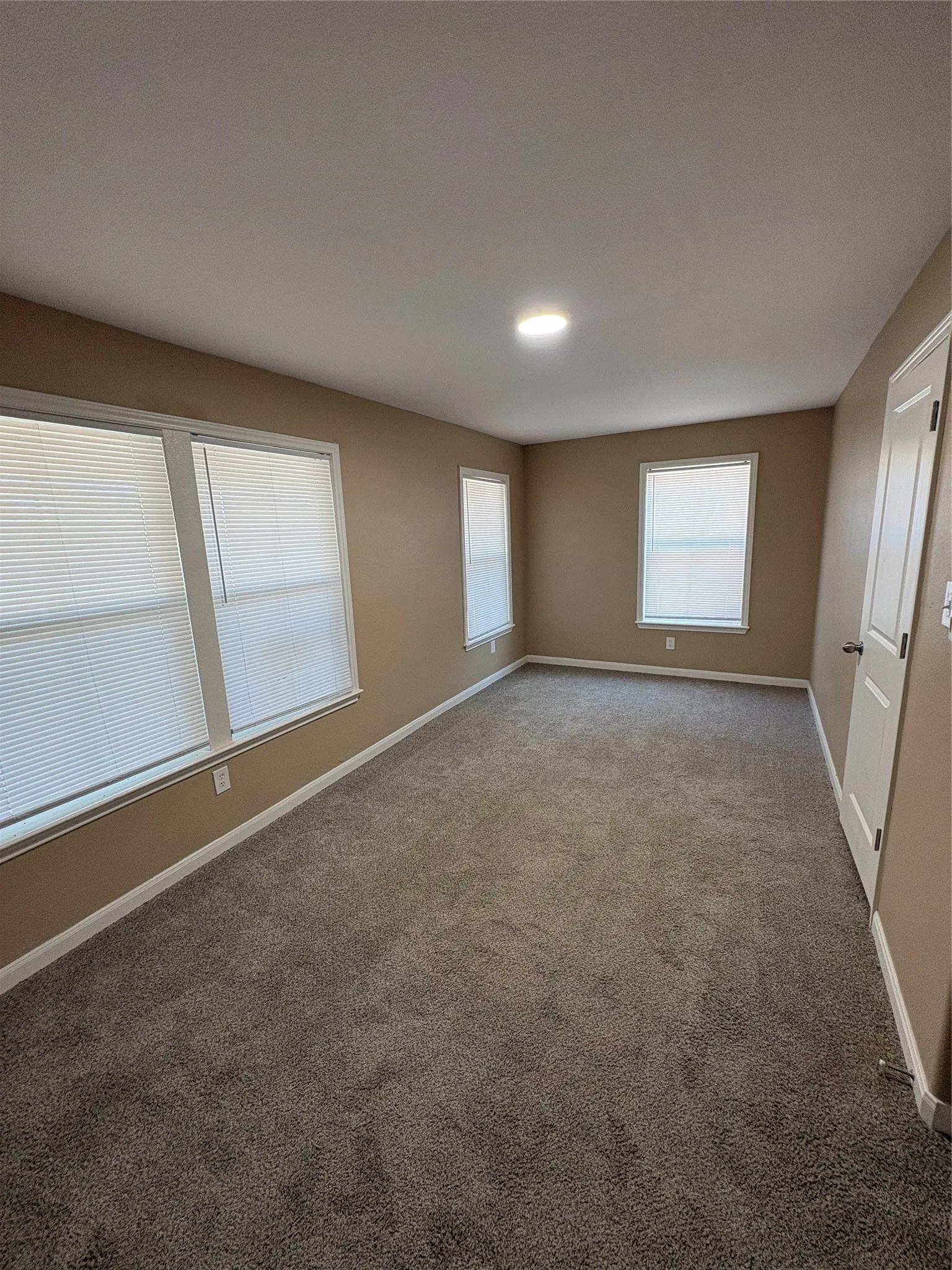 Neutral tone wall paint, recessed lighting, carpet flooring, multiple windows, and a paneled interior door