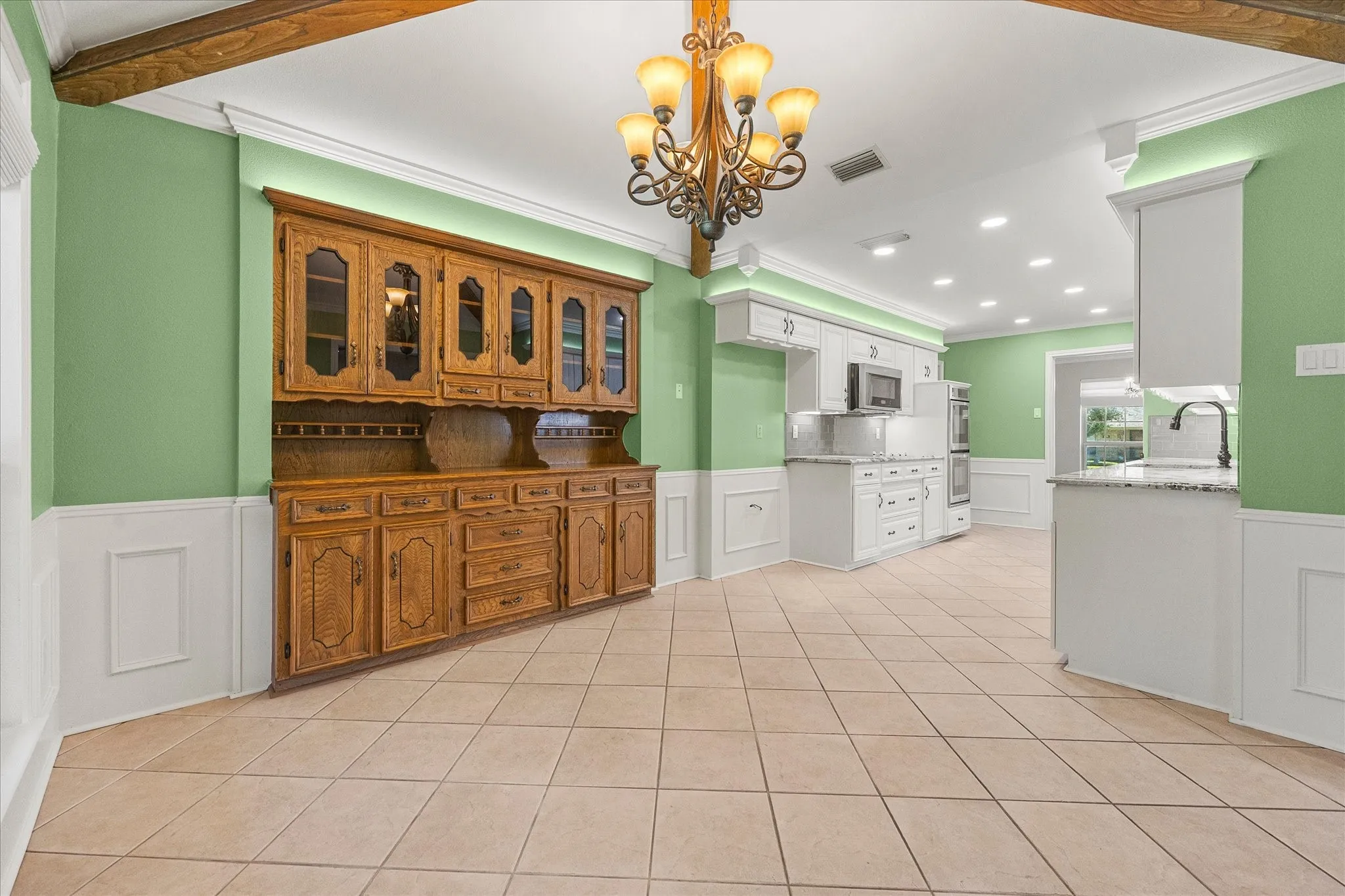 Breakfast and kitchen area featuring a built-in cabinet, decorative lighting, and neutral ceramic tile. While sitting at your breakfast table, you will have a view of the spacious backyard.