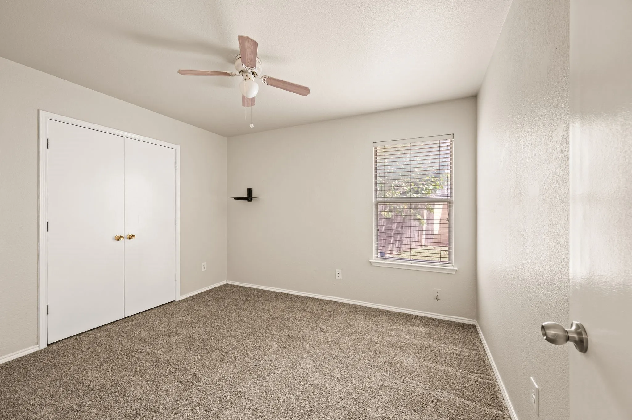Neutral-toned carpeting, ceiling fan with integrated lighting, window with horizontal blinds, bi-fold closet doors, and light-toned walls