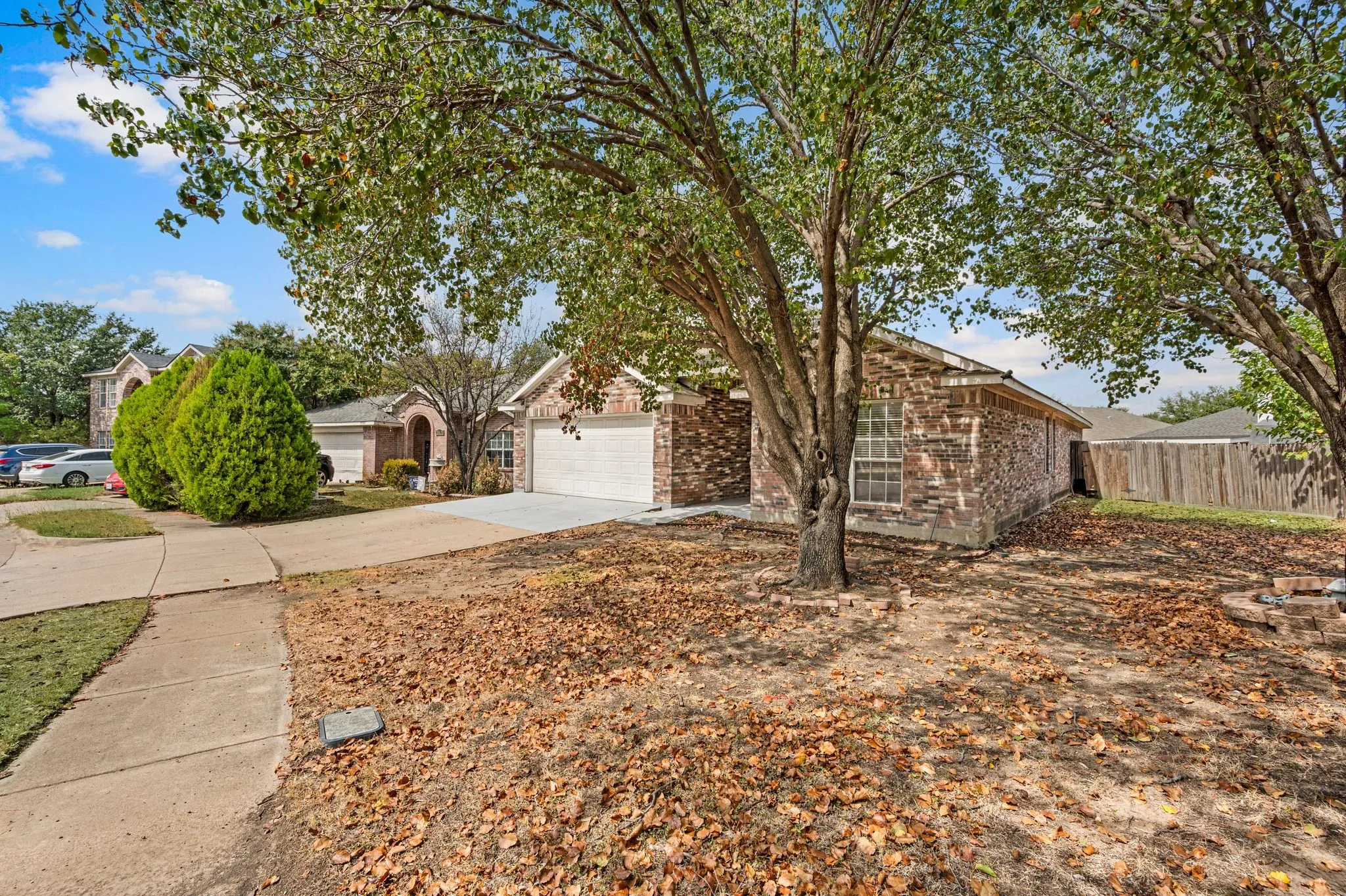 Brick exterior residence with an attached two-car garage, mature shade trees, and a concrete driveway