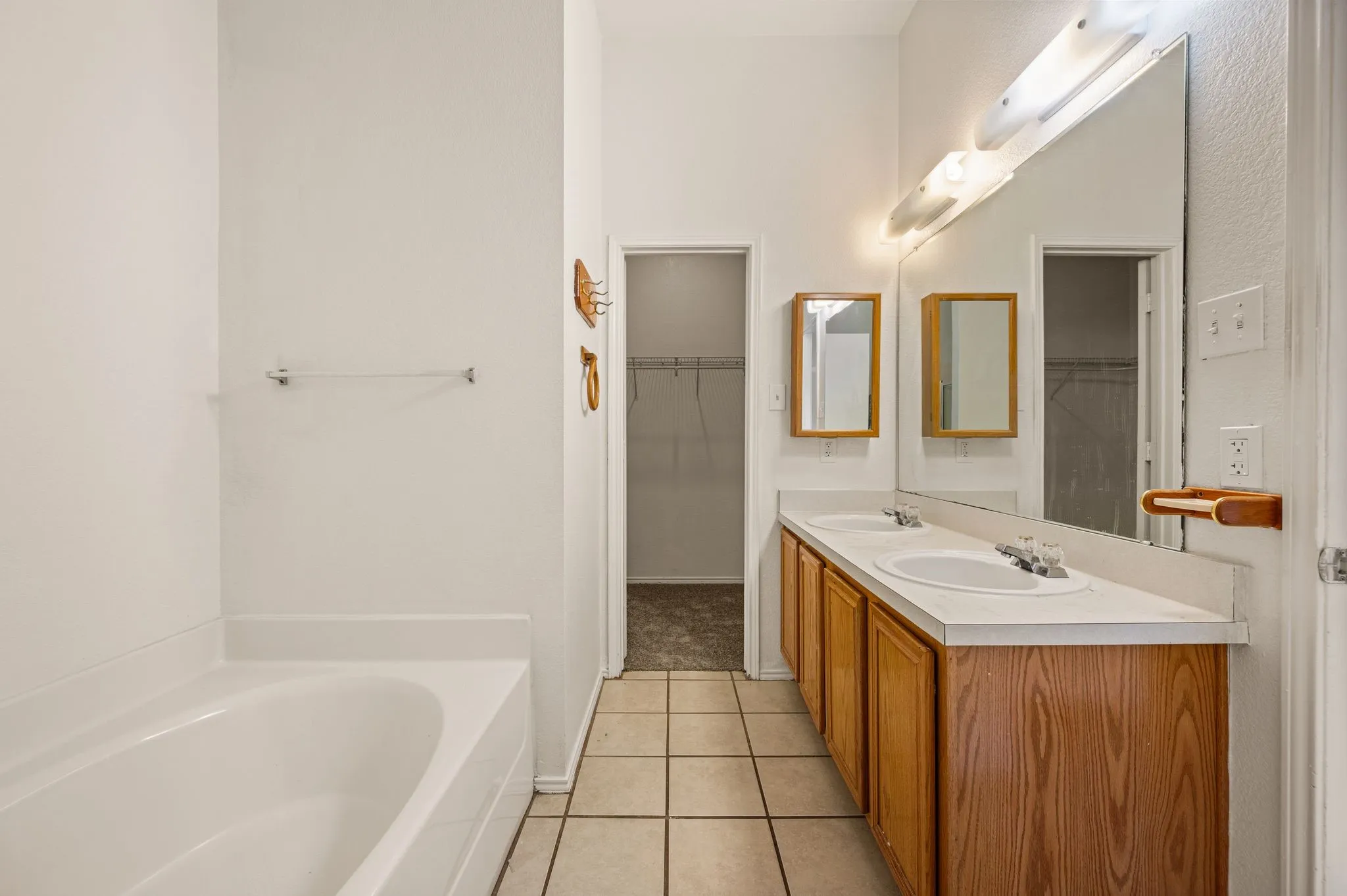 Double vanity with wood-finish cabinetry, tile flooring, built-in bathtub, and an integrated wall mirror