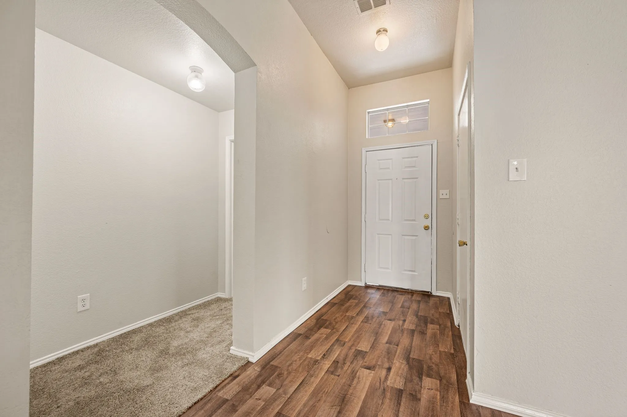 Entryway featuring wood-finish flooring, a white paneled door with a transom window, and an overhead flush mount light fixture
