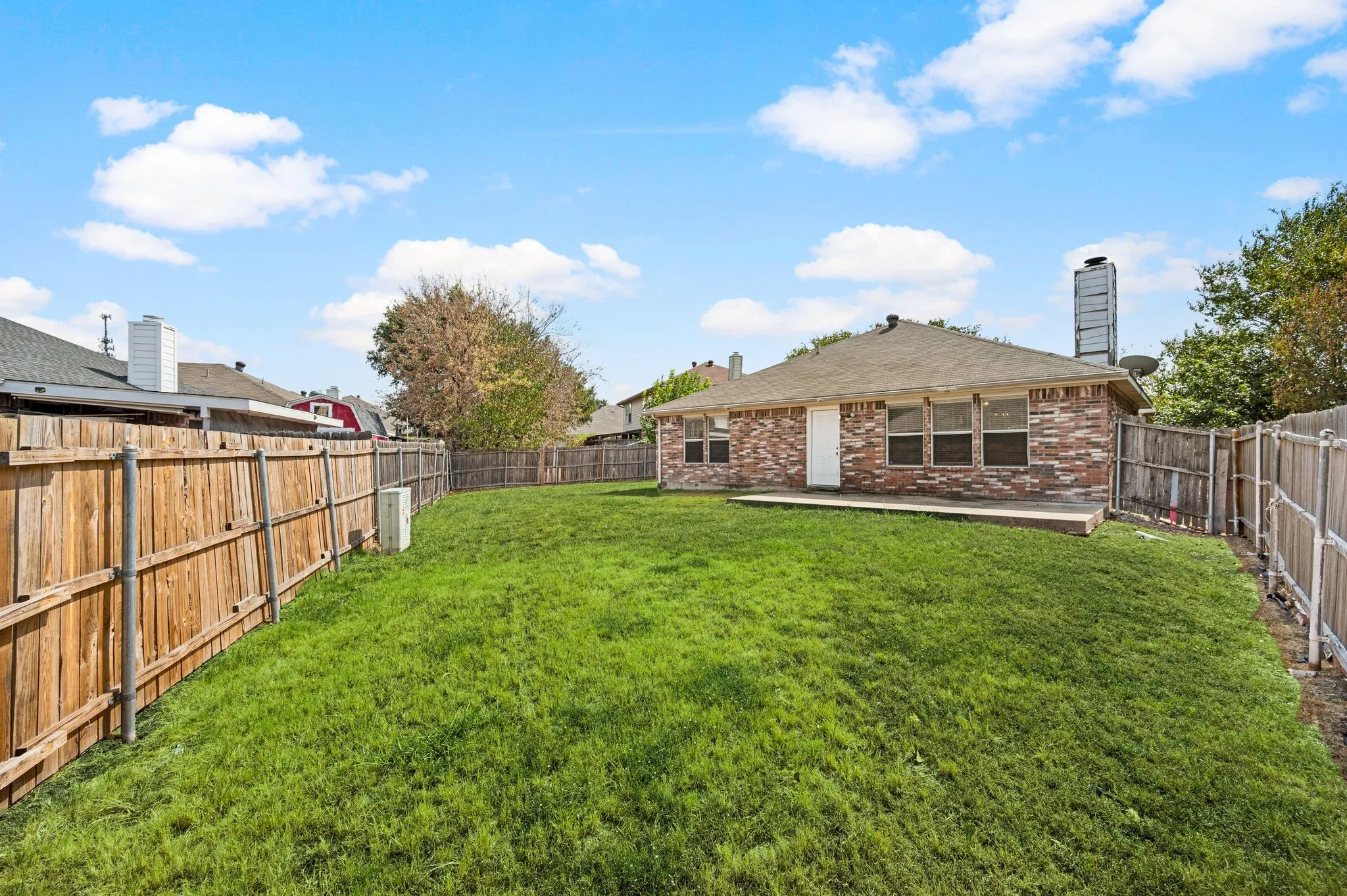 Expansive backyard featuring a manicured lawn, wood fencing, and a brick exterior