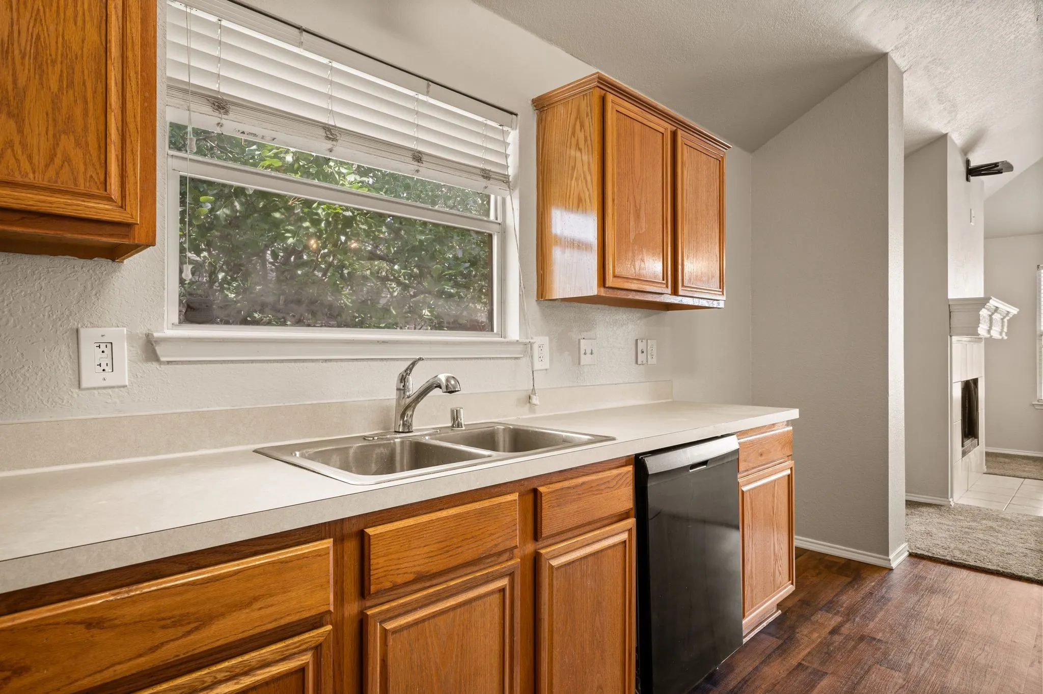 Kitchen featuring wood cabinetry, a dual basin stainless steel sink, a dishwasher, light-toned countertops, and wood-finish flooring