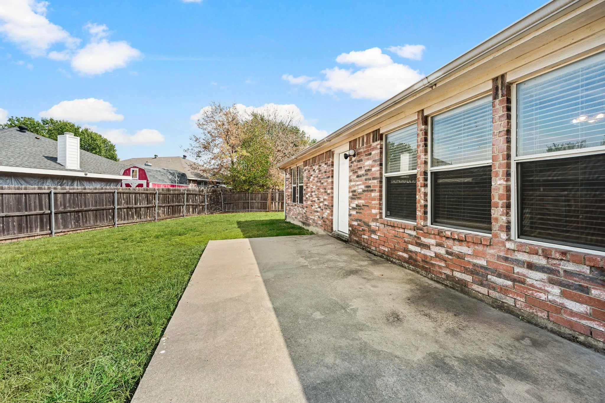 Expansive backyard with a concrete patio, a privacy fence, and a brick exterior