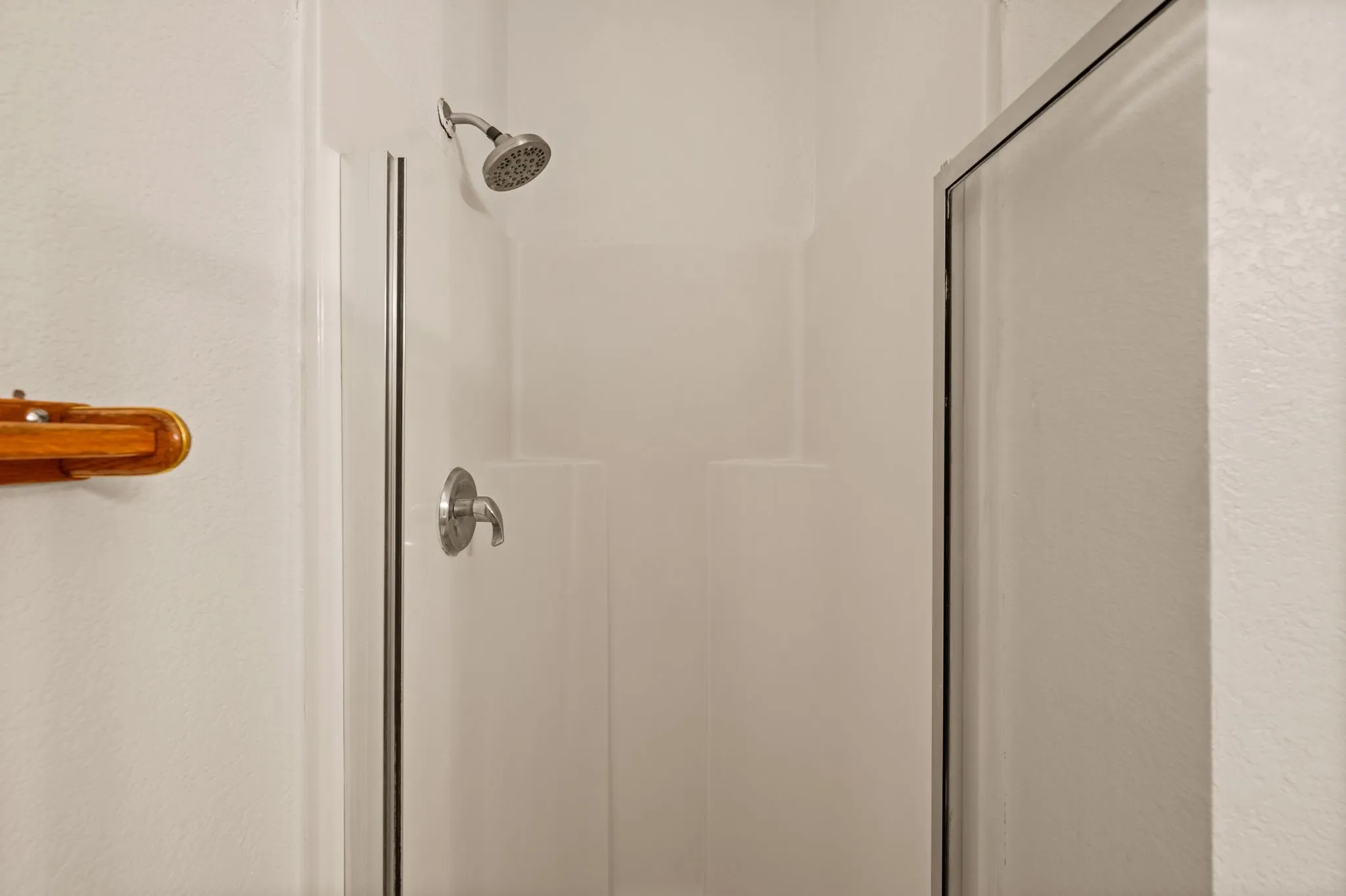 Enclosed shower with a white surround, featuring a chrome showerhead and control handle