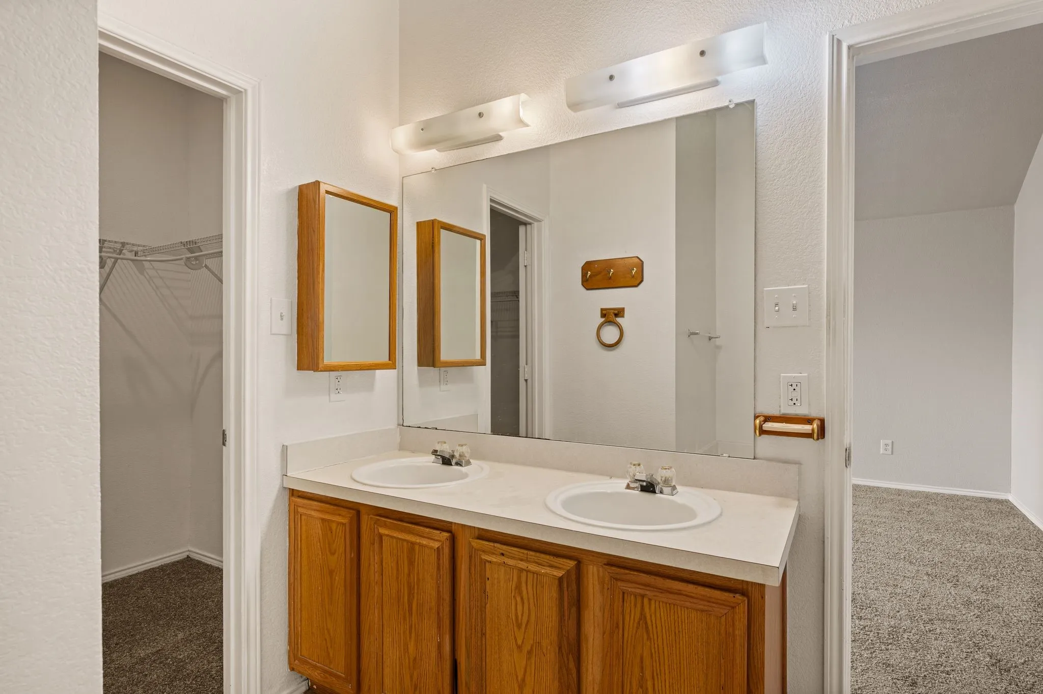 Dual vanity with wood-finish cabinetry and a large wall-mounted mirror