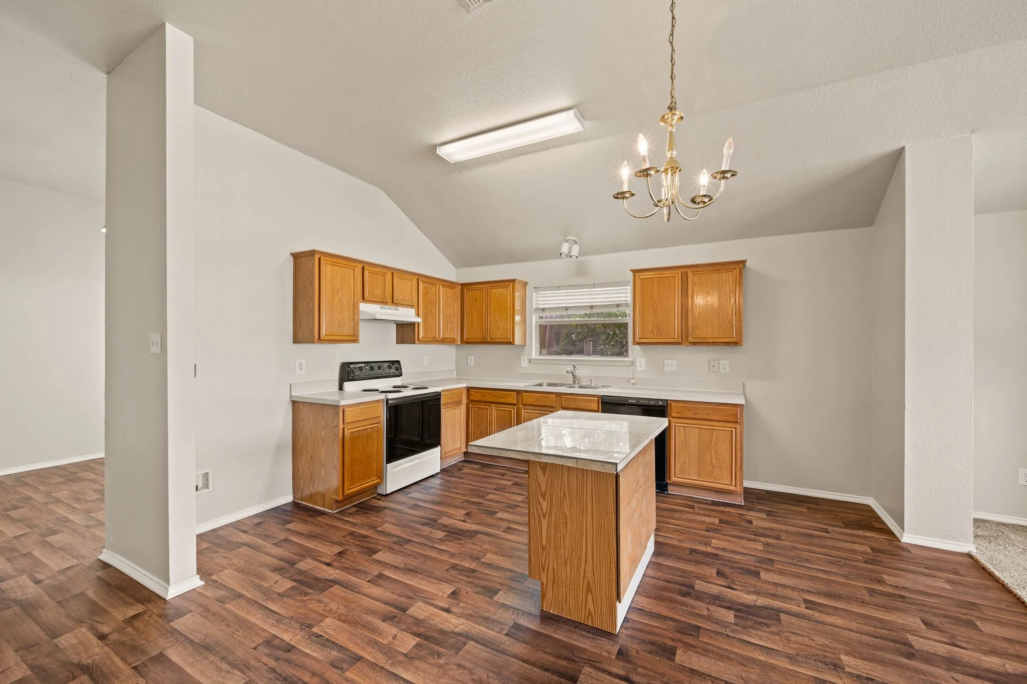 Kitchen featuring wood-finish flooring, a central island with a light-toned countertop, wood cabinetry, built-in appliances, and a vaulted ceiling