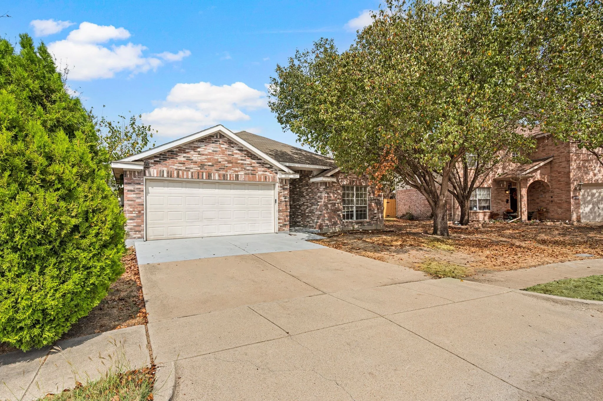 Brick exterior with a gabled roofline, attached garage, and mature landscaping