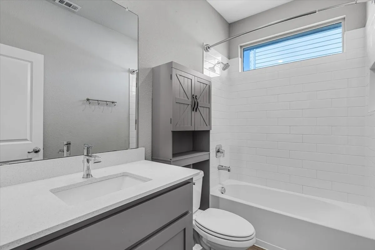 Integrated bathtub with white subway tile surround, quartz countertop vanity with undermount sink, gray vanity cabinetry, and a horizontal transom window
