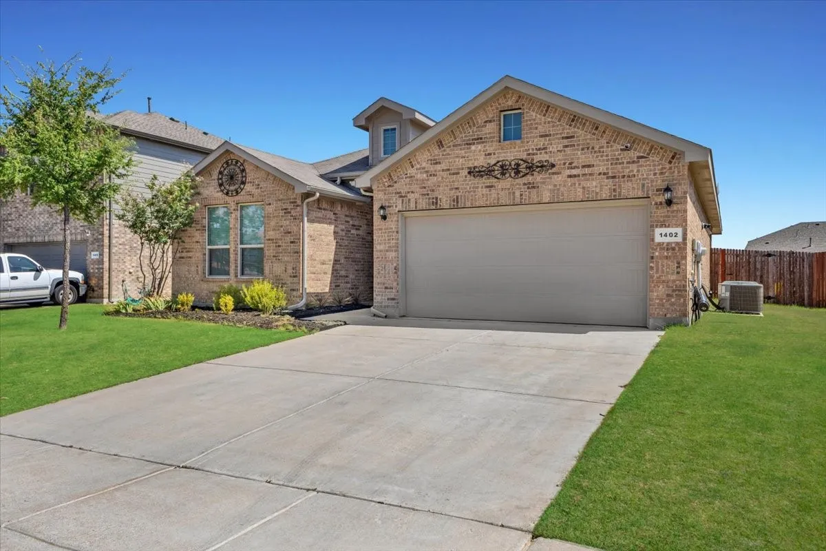 Brick exterior with decorative accents, an attached garage, a concrete driveway, and a front lawn with landscaping
