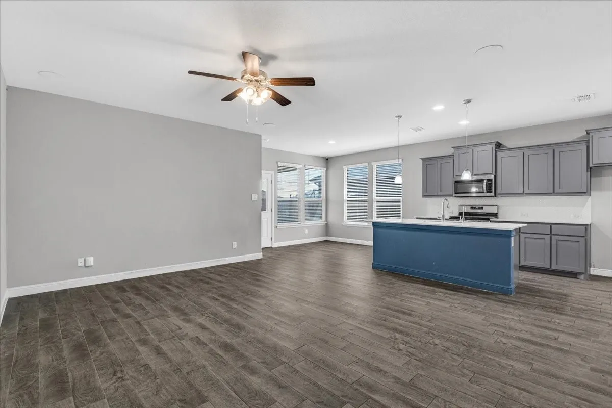 Open-concept living area with wood-finish flooring, a ceiling fan, and multiple windows