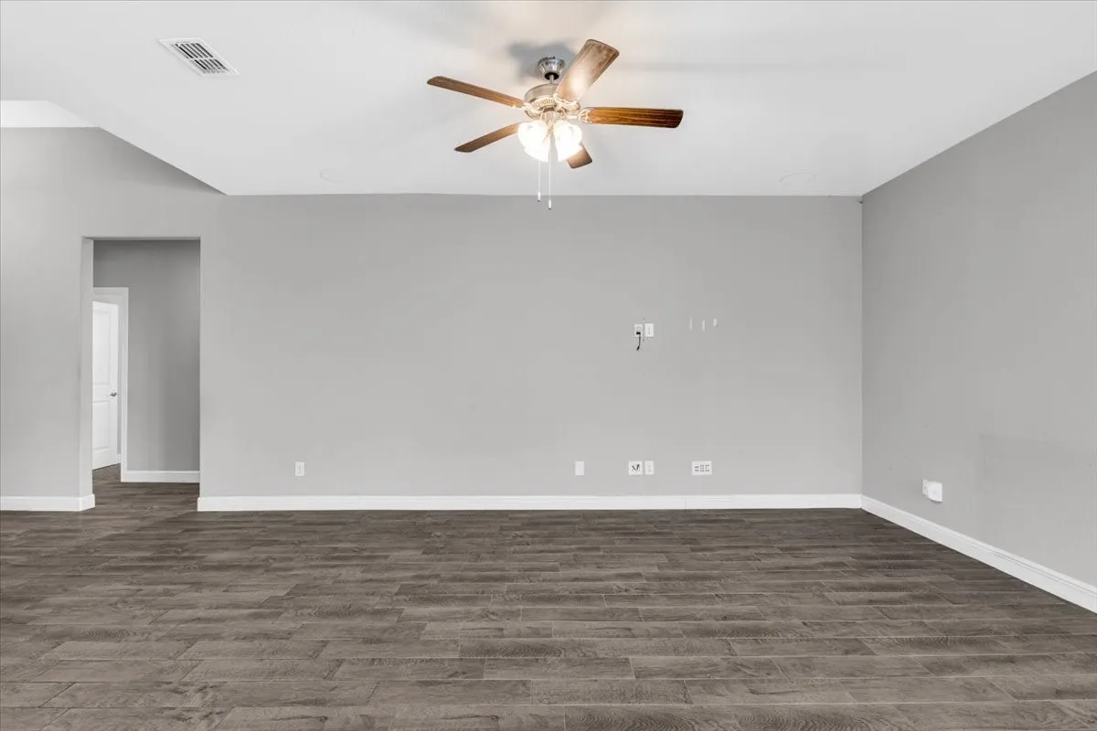 Spacious interior with wood-finish flooring, light grey walls, and a ceiling fan with integrated lighting