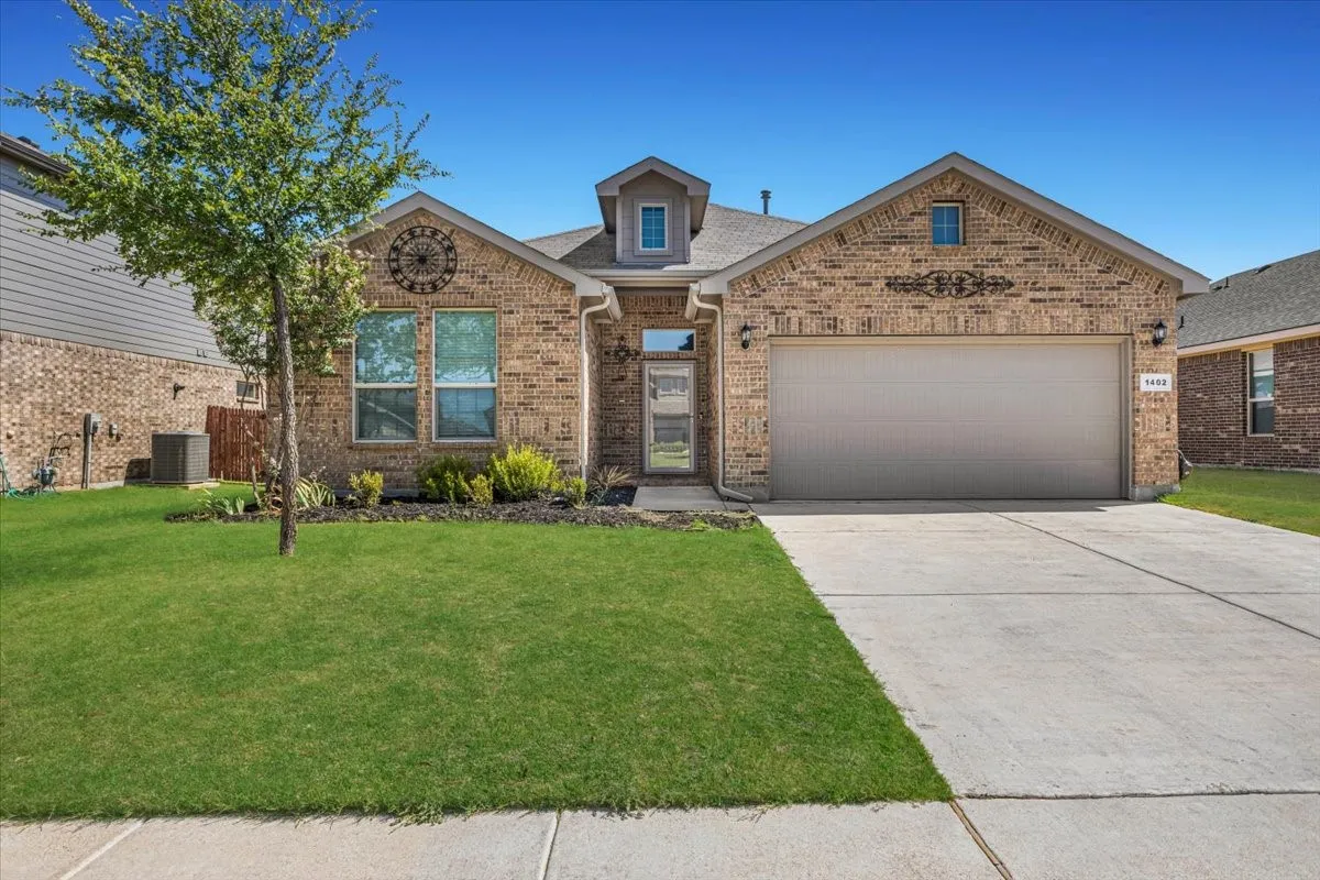 Brick exterior with a dormer, an attached garage, a concrete driveway, and a manicured lawn