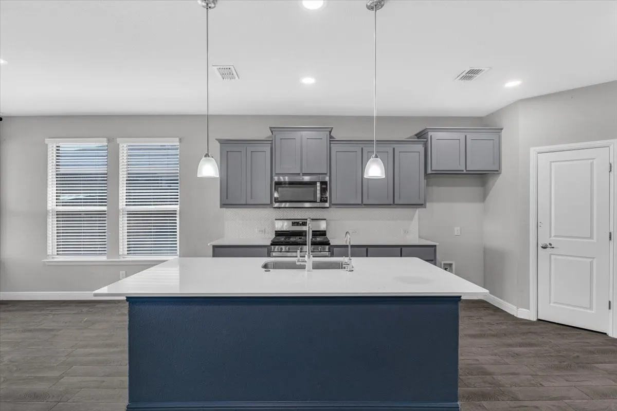 Kitchen featuring a large island, gray cabinetry, stainless steel appliances, and wood-finish flooring