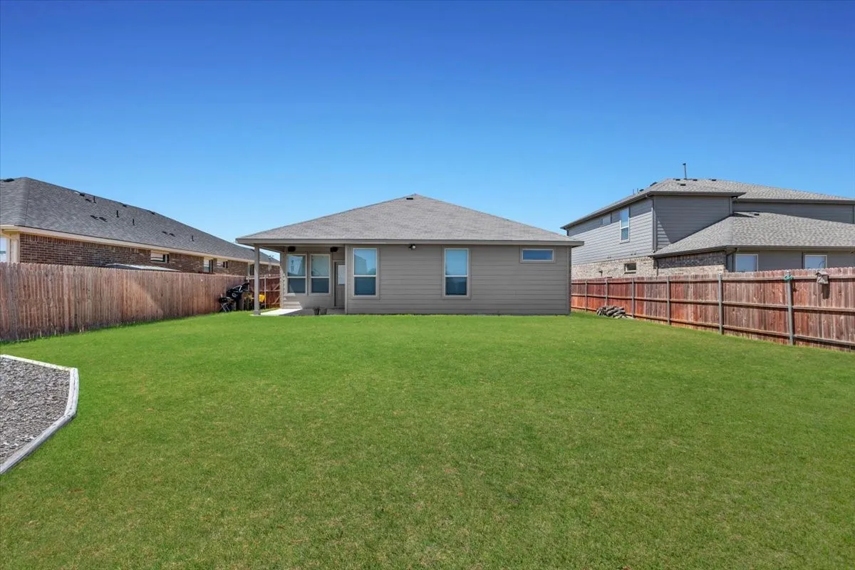 Expansive green lawn, wood privacy fencing, covered patio, tan exterior siding, and multiple windows