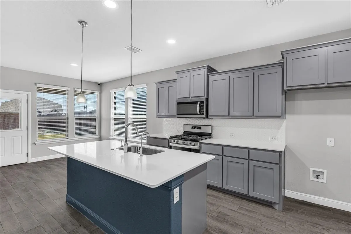 Modern kitchen featuring a central island with a sink, stainless steel appliances, grey cabinetry, white countertops, and wood-finish flooring