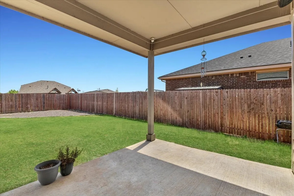 Covered concrete patio with a spacious grass lawn and privacy fencing