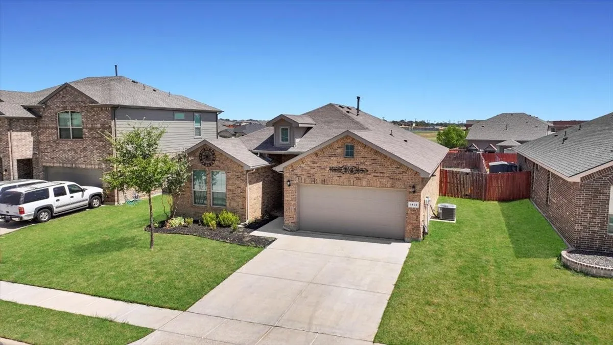 Brick exterior with an attached garage, paved driveway, and a front yard with mature landscaping