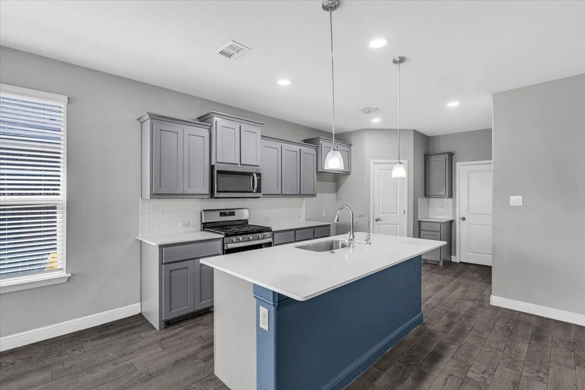 Kitchen featuring a central island with an undermount sink, pendant lighting, wood-finish flooring, gray cabinetry, and white countertops