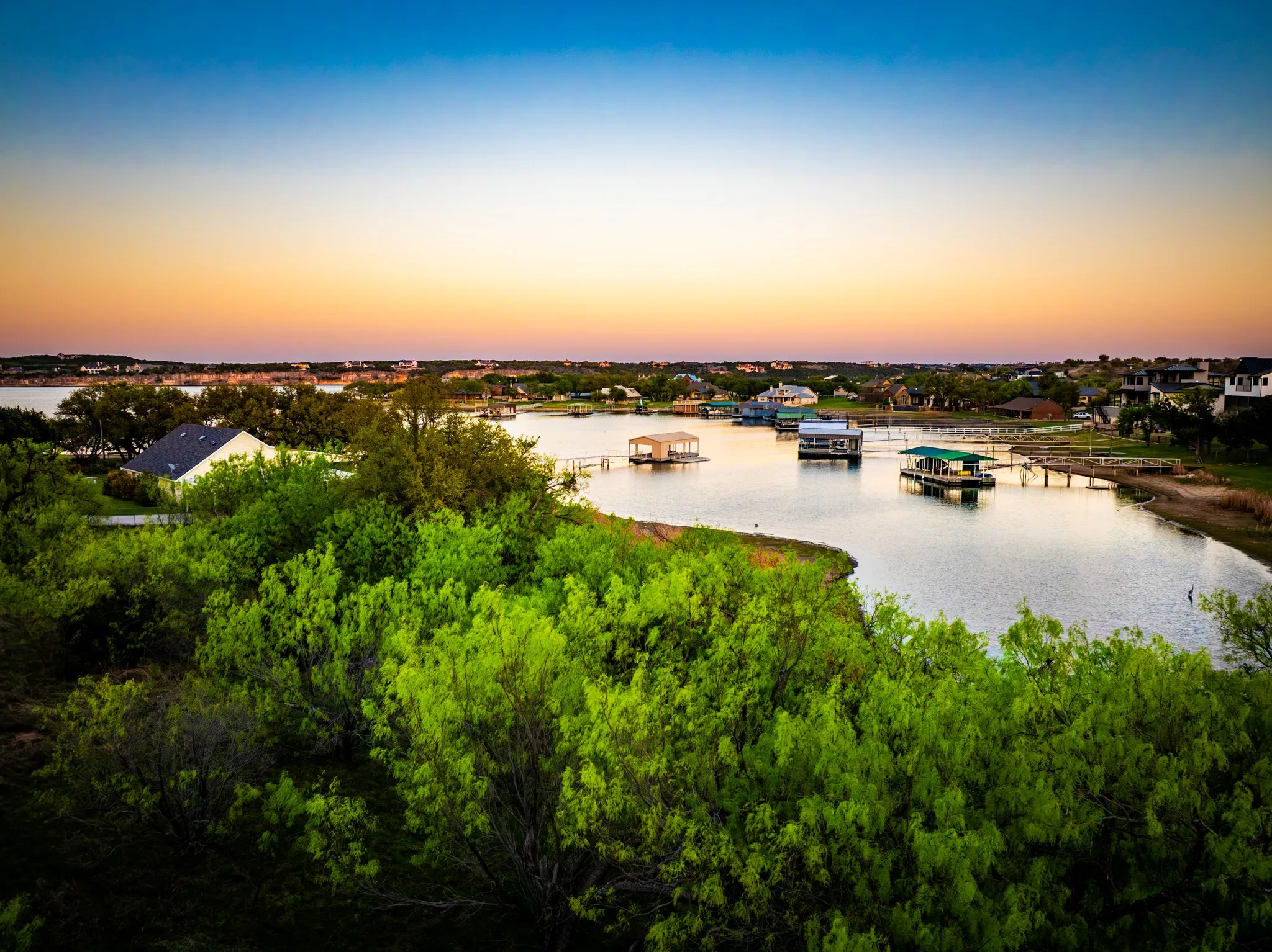 Waterfront property with established greenery, a visible boat dock, and surrounding residential structures
