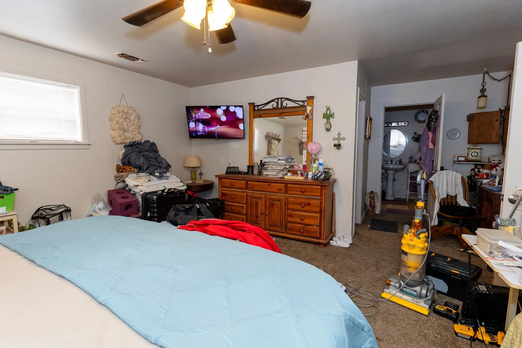 Window with blinds, ceiling fan with integrated lighting, wall-mounted television, wood-finish dresser with mirror, and carpeted flooring