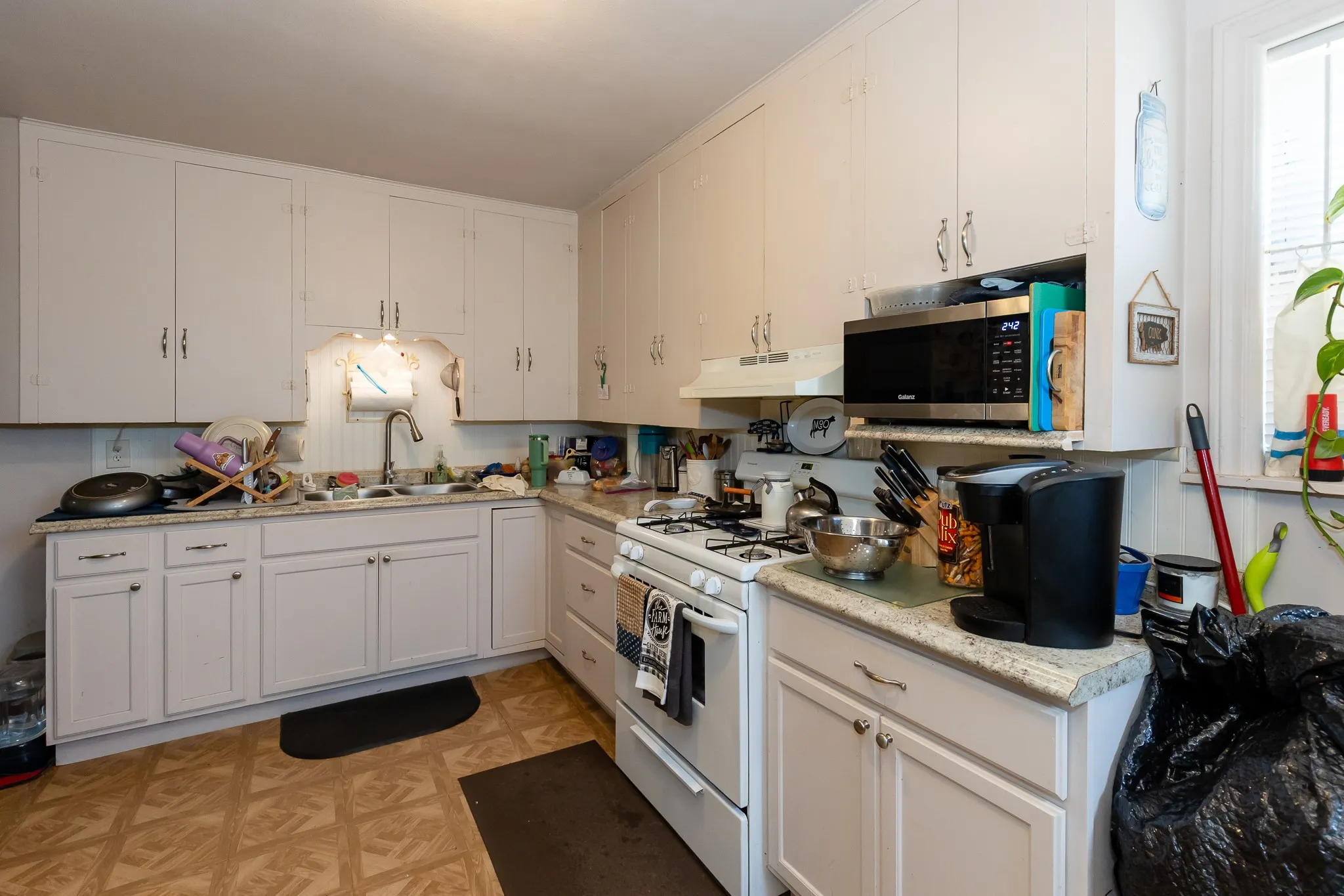 Bright, functional kitchen featuring white cabinetry with hardware accents, wood-finish flooring, and stainless steel appliances including a gas range