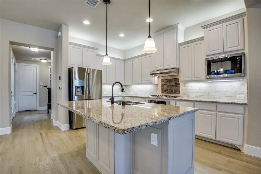 Kitchen with white cabinetry, granite countertops, stainless steel appliances, and wood-finish flooring