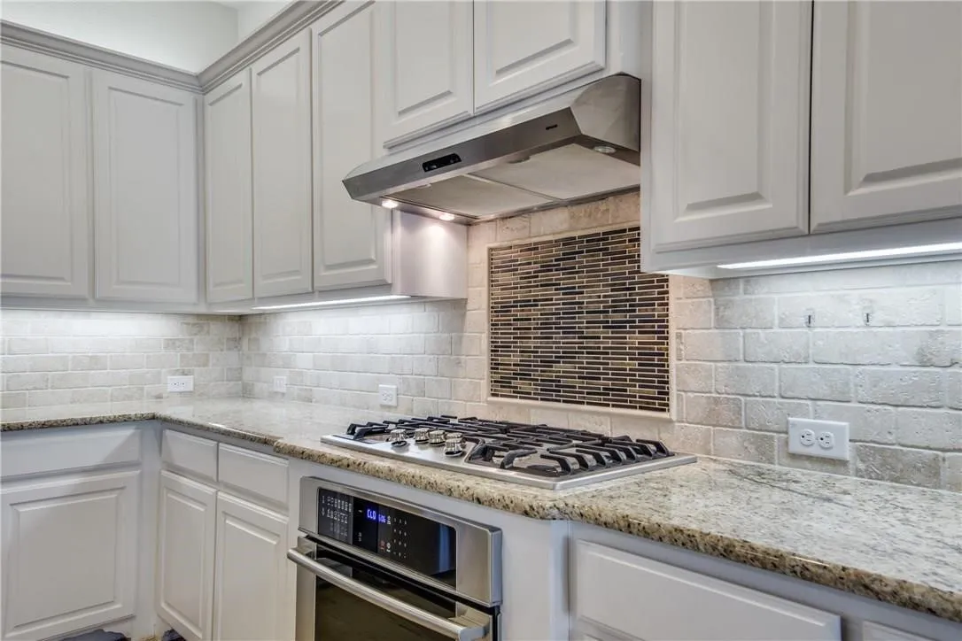Custom cabinetry with crown molding, granite countertops, tile backsplash, built-in stainless steel oven, and stainless steel gas cooktop