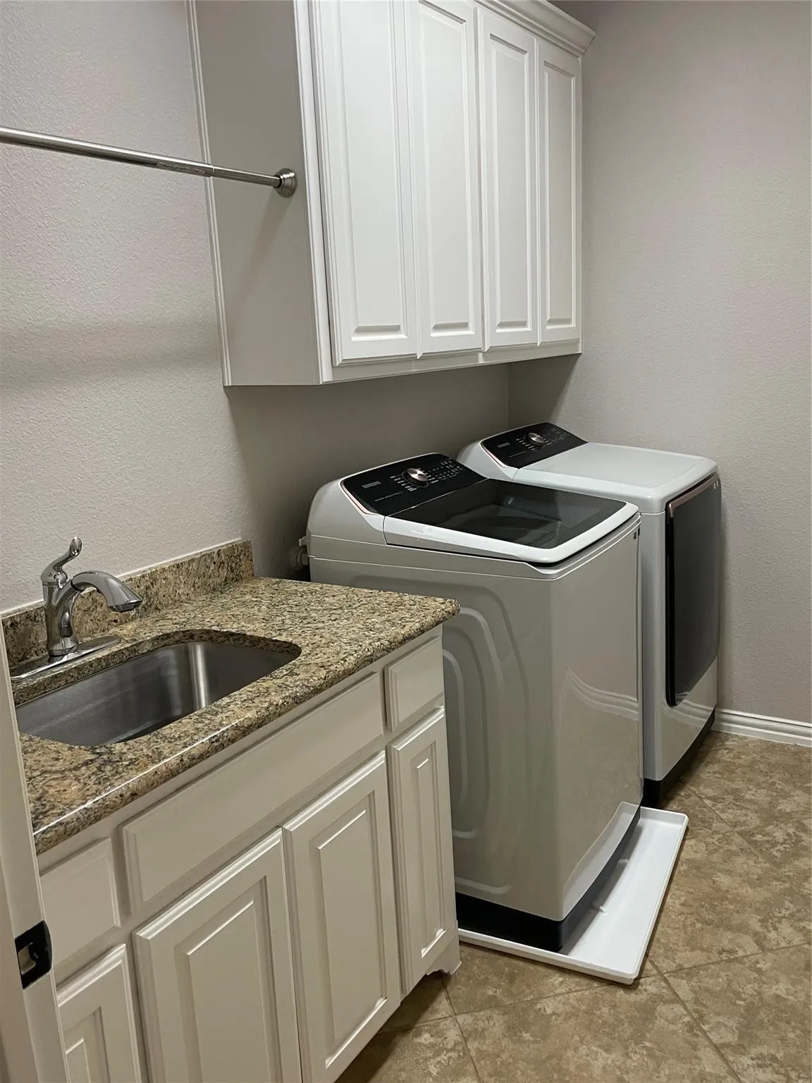 White shaker-style cabinetry, granite-finish countertop, stainless steel sink, and durable tile flooring