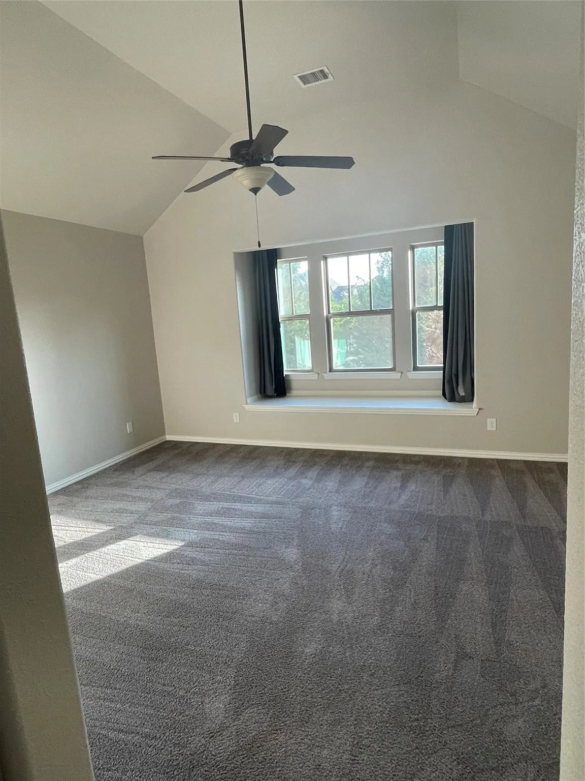 Vaulted ceiling with an attached ceiling fan, large window with a built-in window seat, and carpet flooring