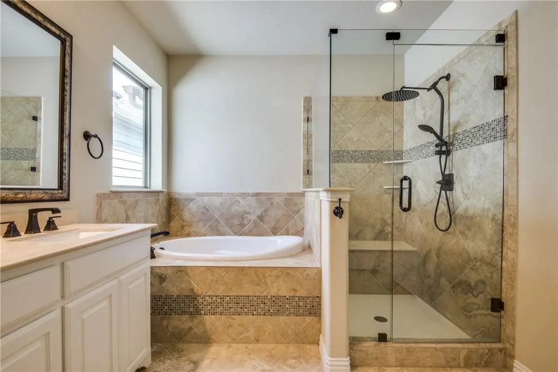Glass-enclosed shower with a built-in bench, a separate oval soaking tub, a single vanity with a solid surface countertop, and tiled walls with decorative accents