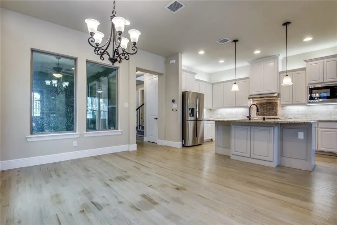 Open-concept living space featuring wood-finish flooring, a contemporary chandelier, and a kitchen with white cabinetry, a large island, and pendant lighting